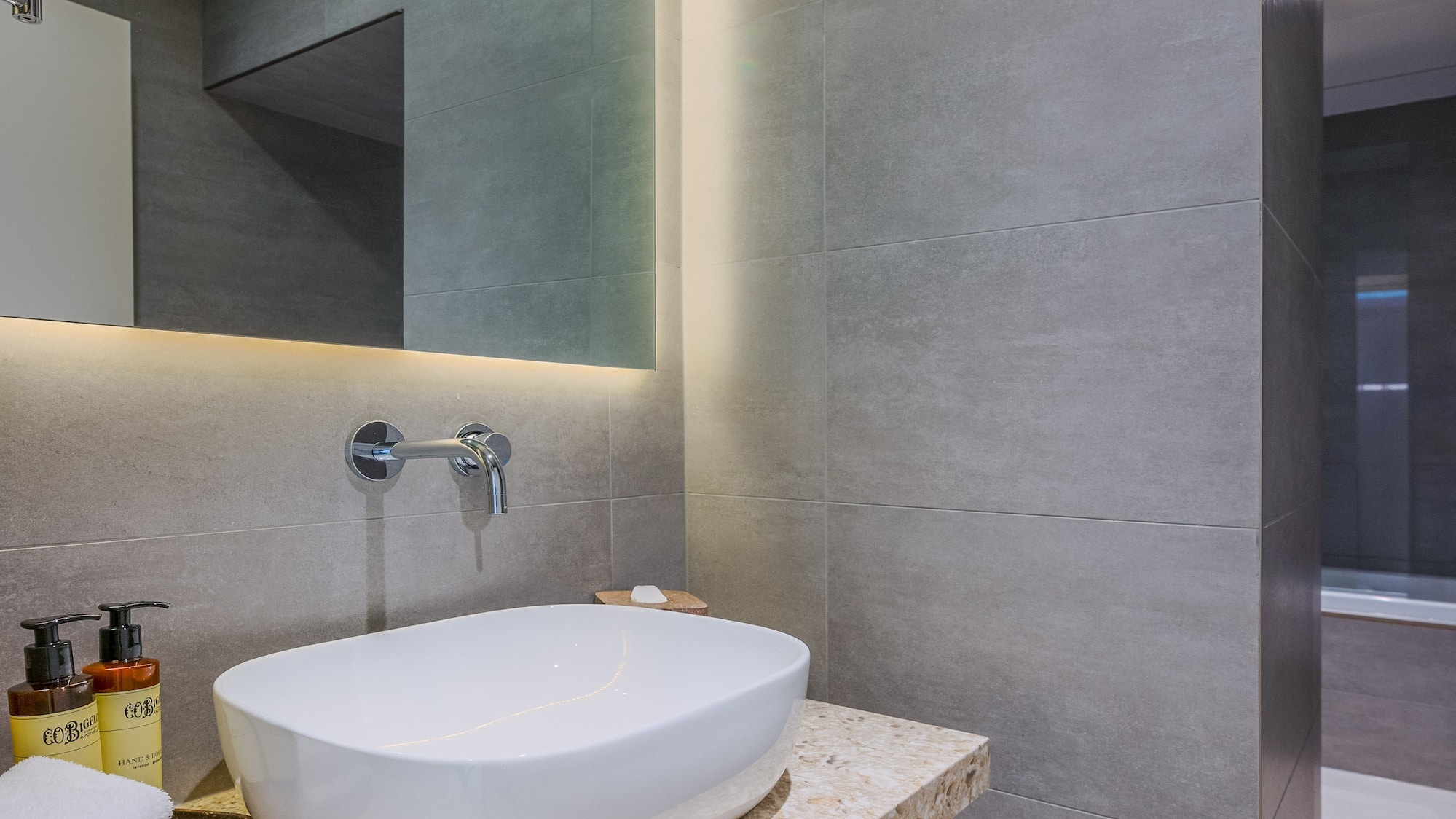 Modern bathroom vanity with white vessel sink, LED mirror, and gray tiles.