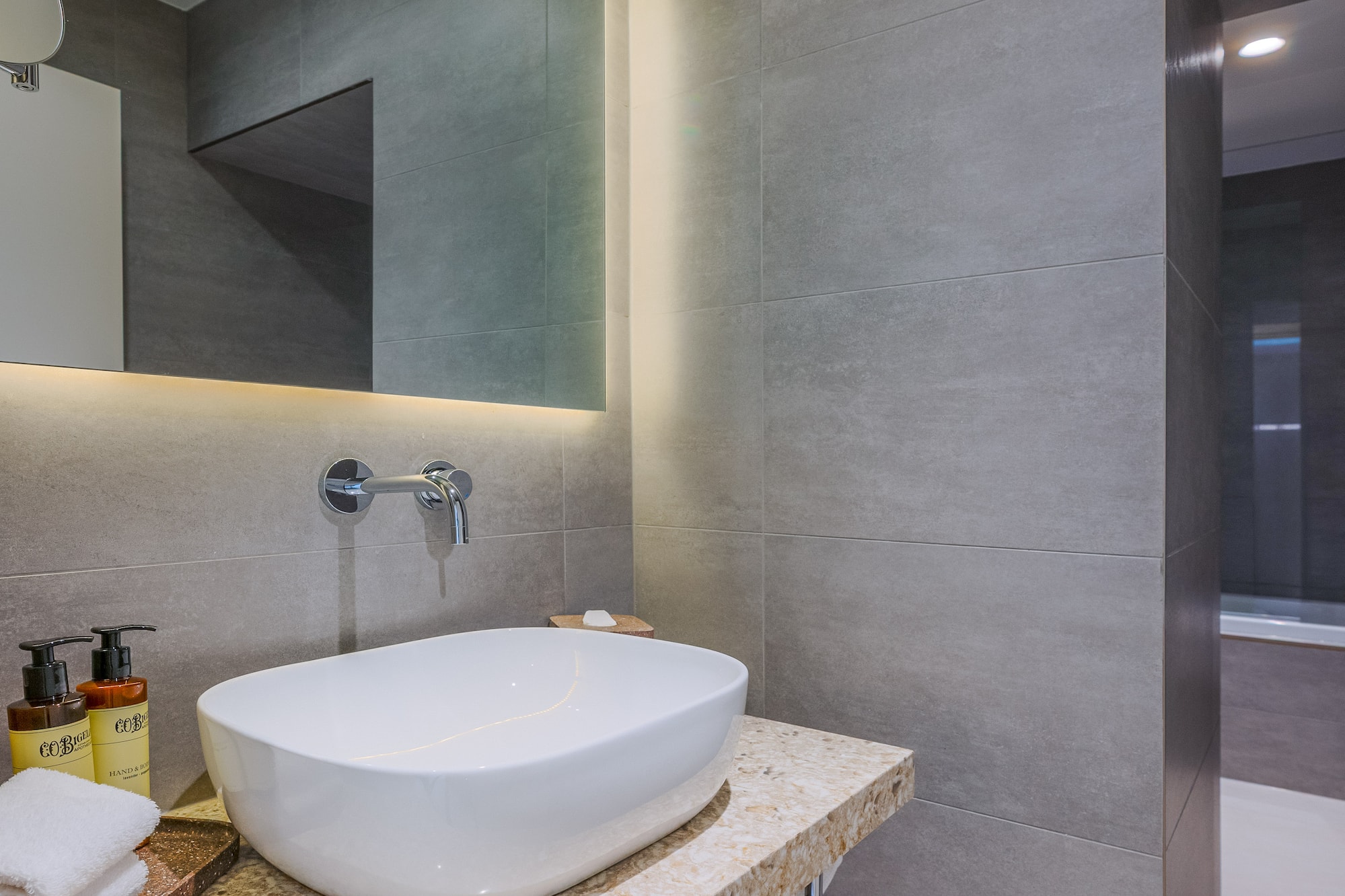 Modern bathroom vanity with white vessel sink, LED mirror, and gray tiles.