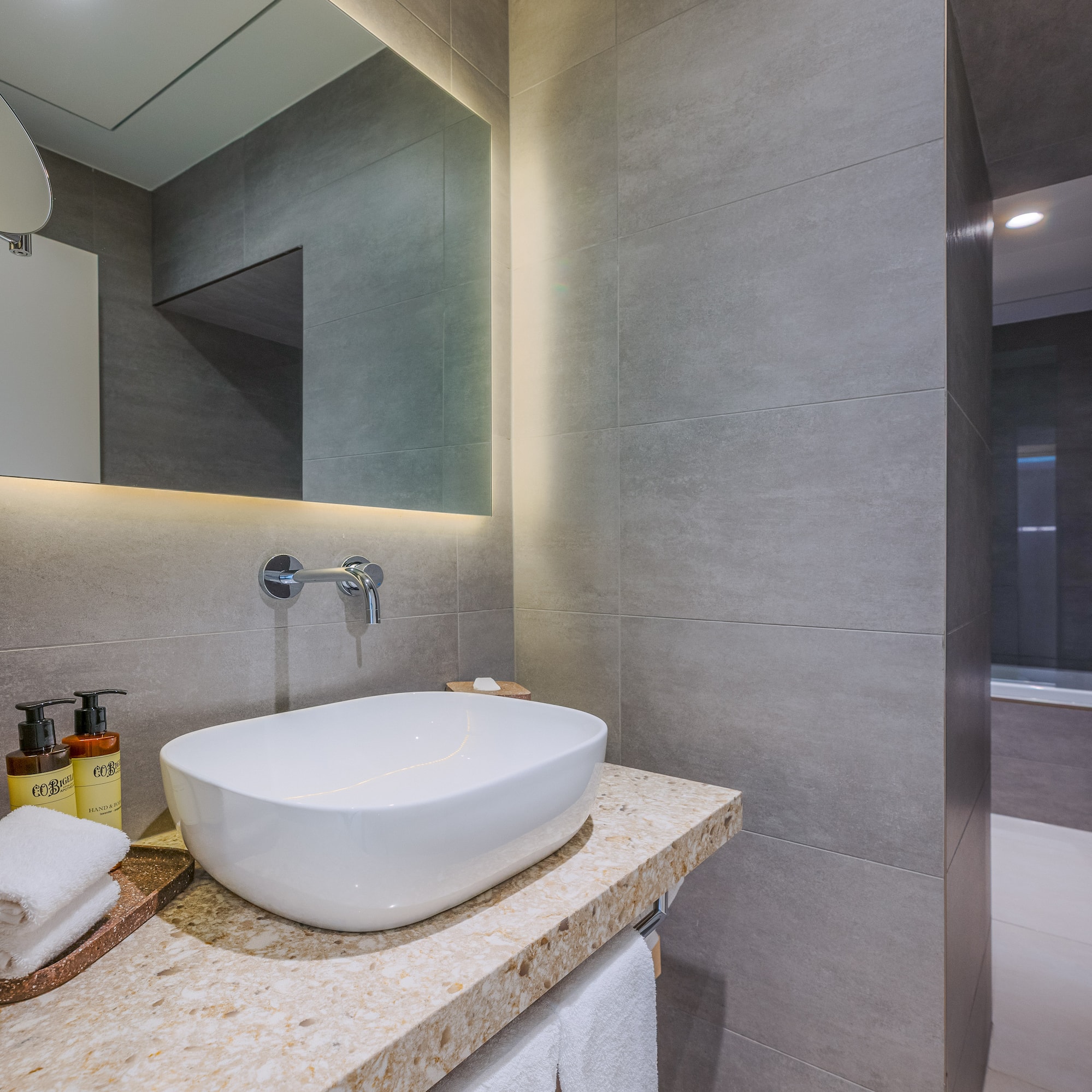 Modern bathroom vanity with white vessel sink, LED mirror, and gray tiles.