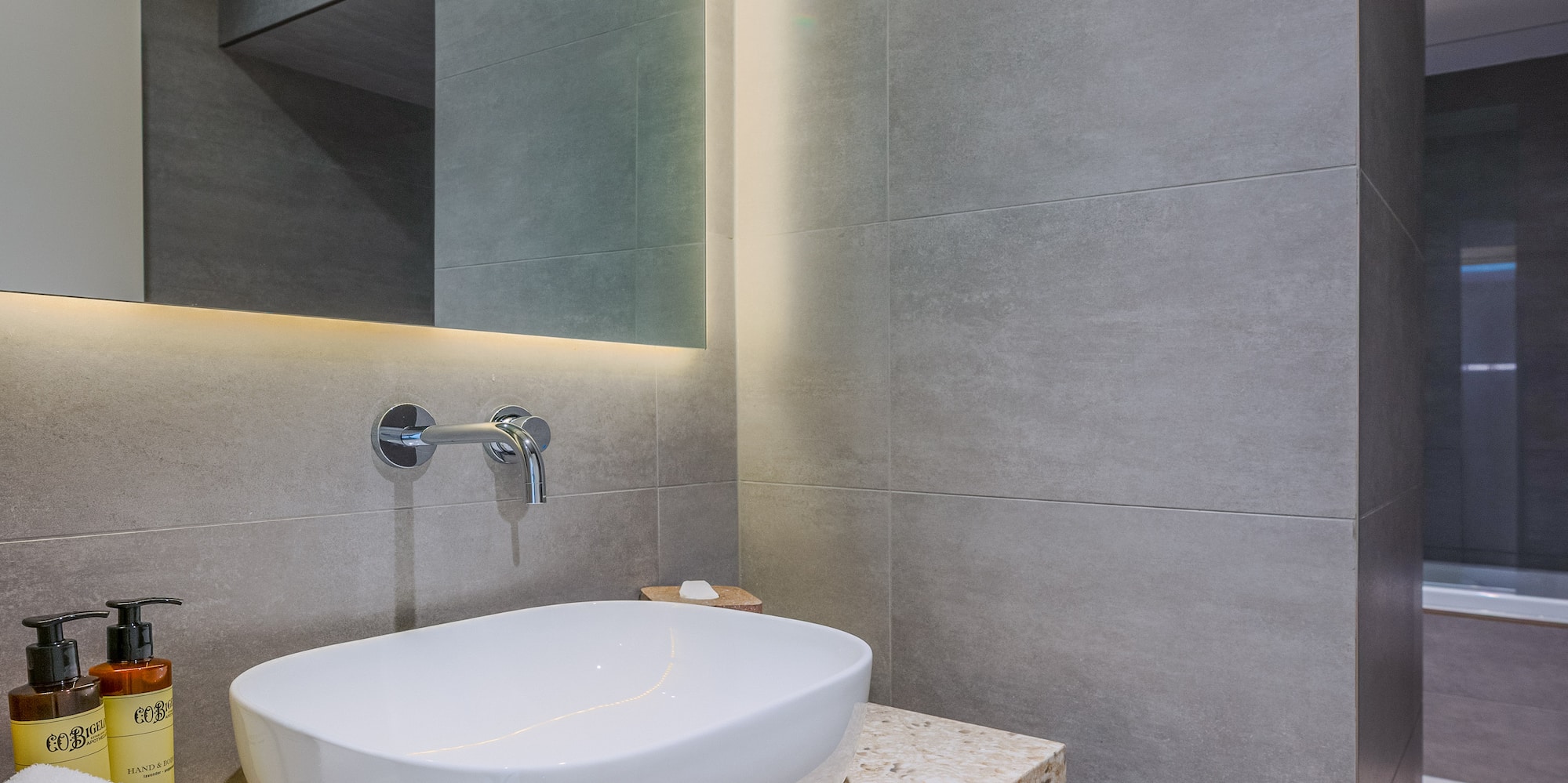 Modern bathroom vanity with white vessel sink, LED mirror, and gray tiles.