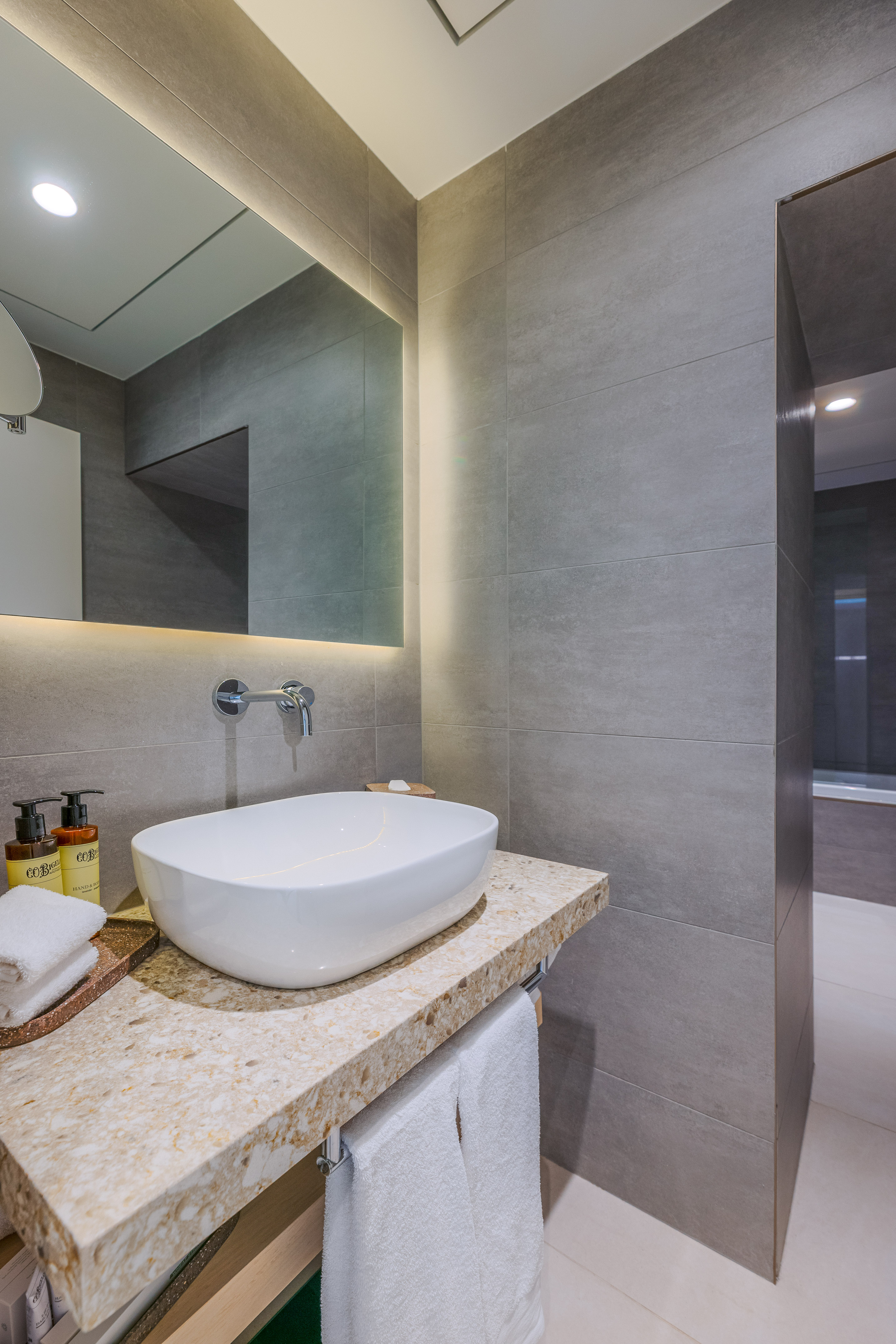 Modern bathroom vanity with white vessel sink, LED mirror, and gray tiles.