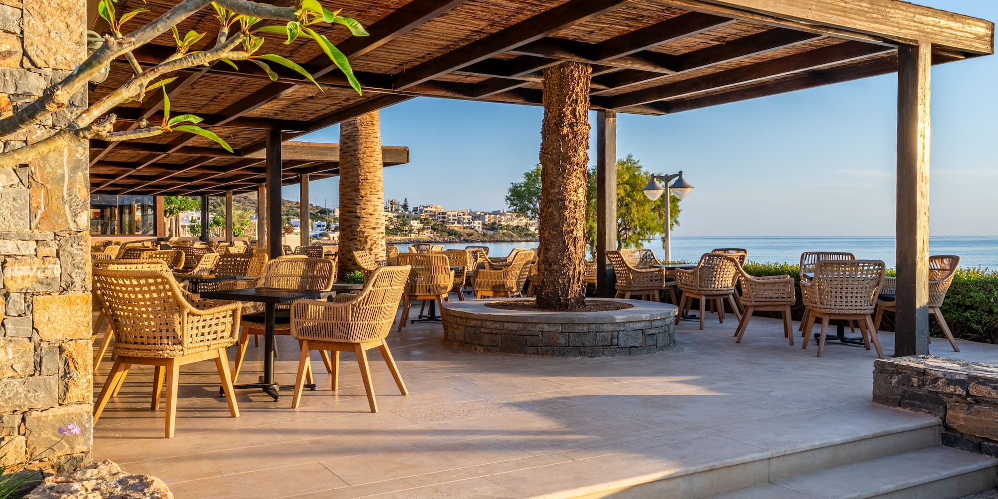 Coastal resort patio with wicker chairs and pergola, overlooking the sea.