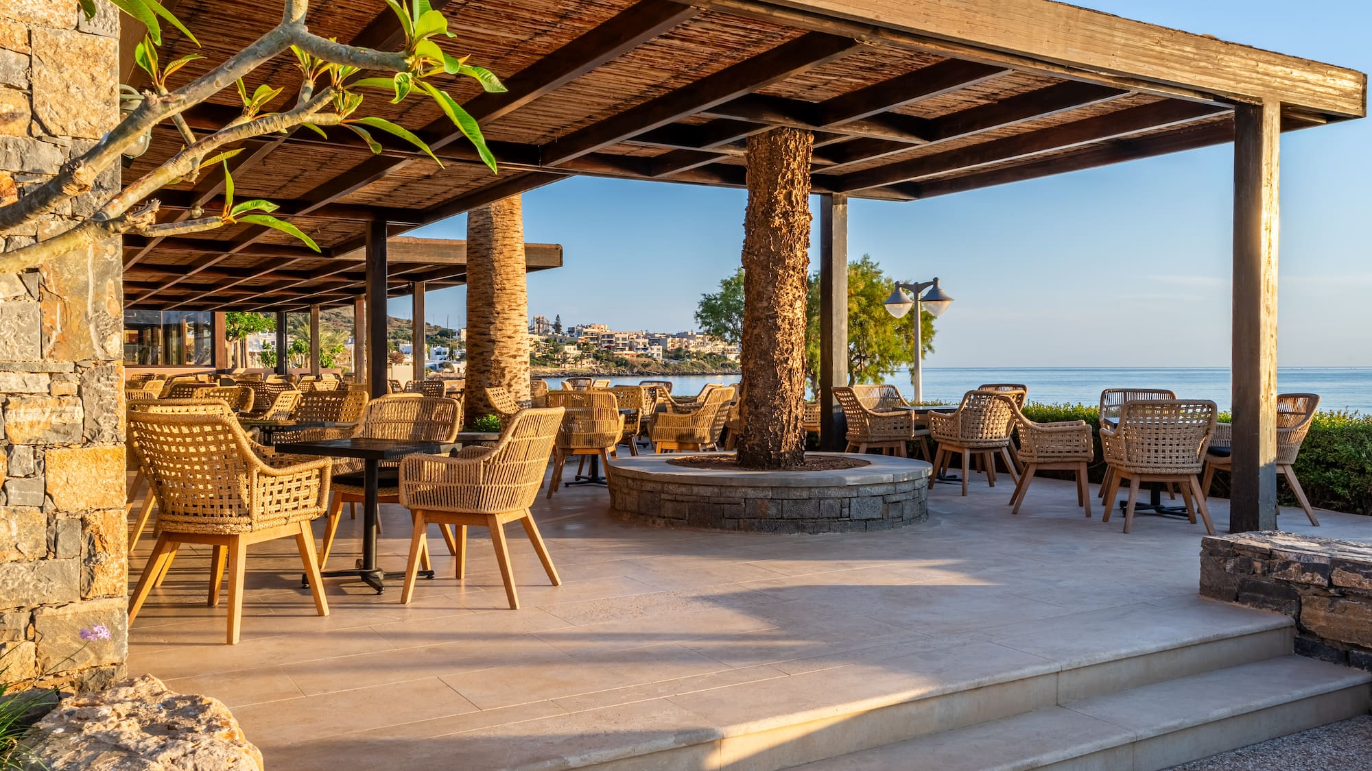 Coastal resort patio with wicker chairs and pergola, overlooking the sea.