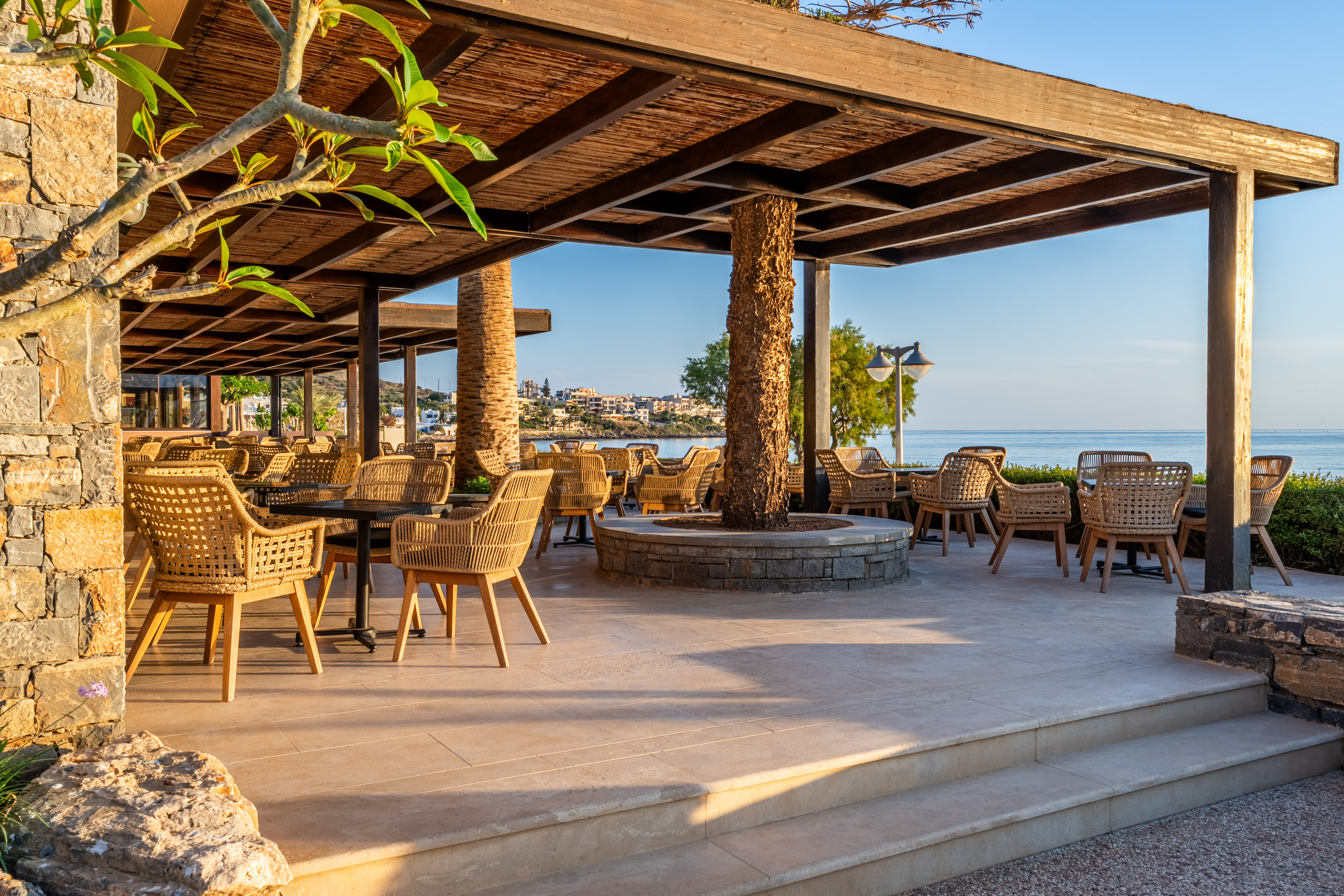 Coastal resort patio with wicker chairs and pergola, overlooking the sea.