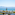 Balcony sea view of coastal buildings, distant mountains, and a tall pine tree.