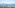 Balcony sea view of coastal buildings, distant mountains, and a tall pine tree.