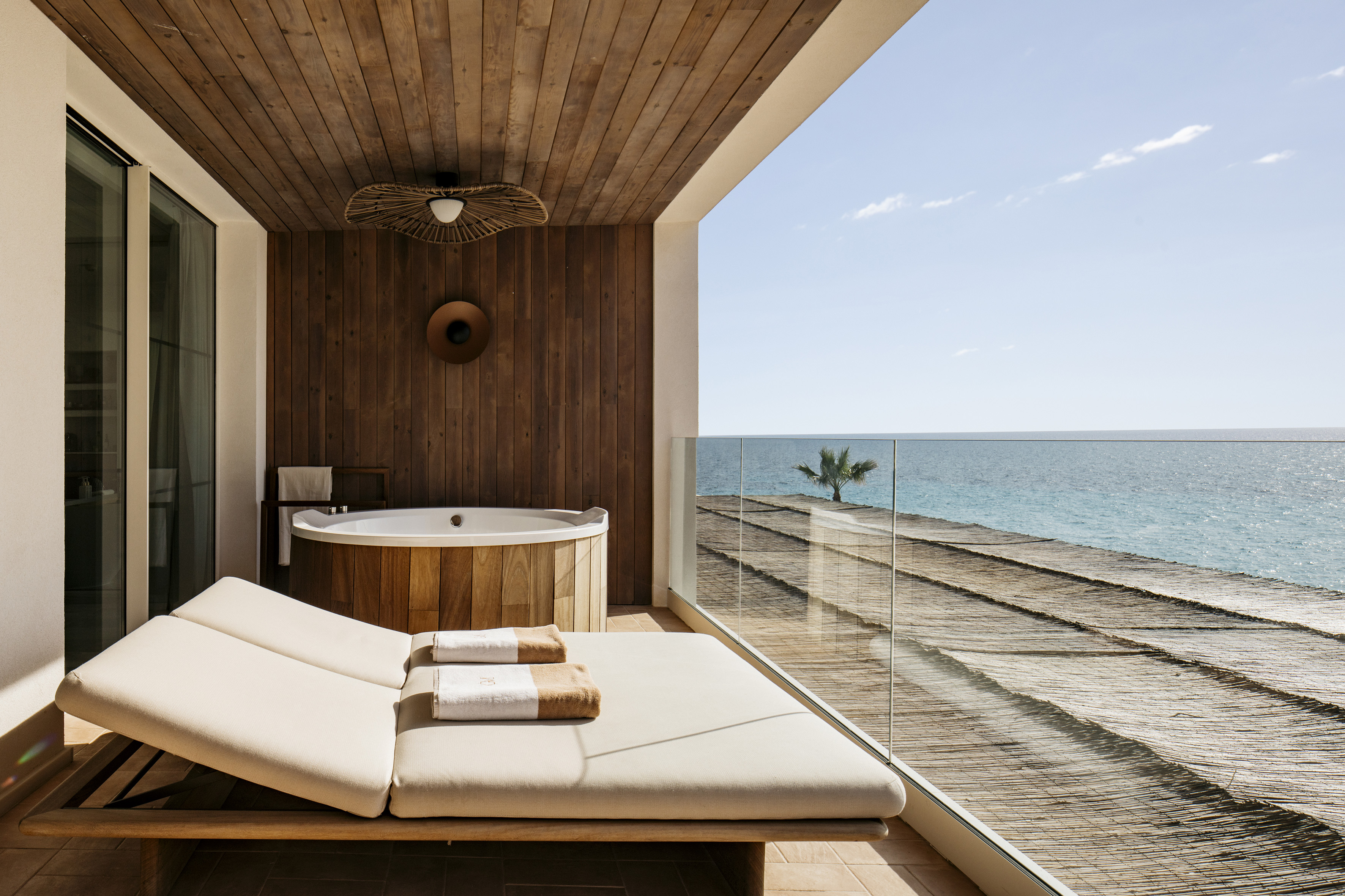 Private balcony with wooden hot tub, daybed, and sea view.
