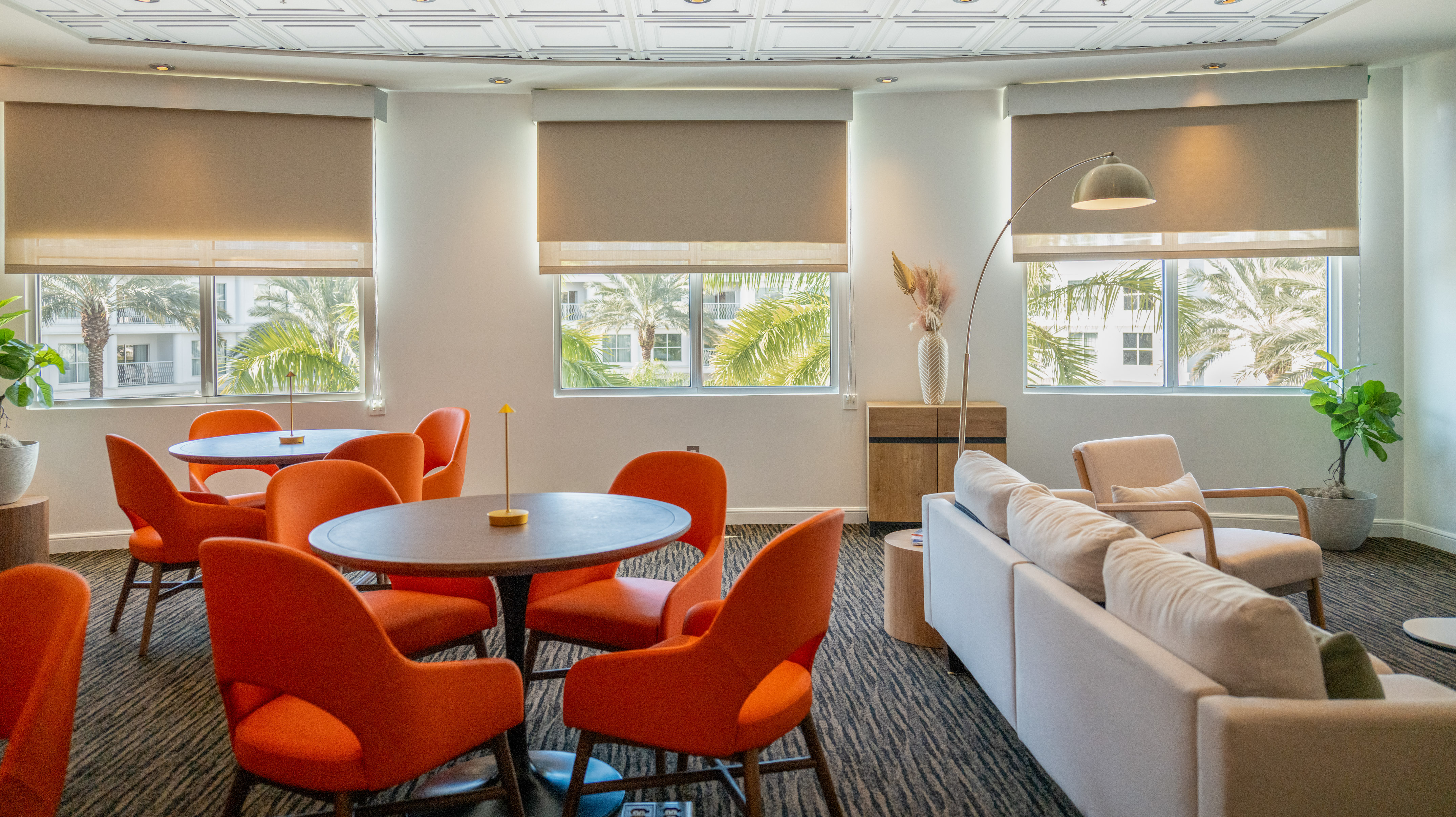 Lounge area with orange chairs, white sofa, and windows overlooking palm trees. - The Level - Meliá Orlando Celebration, Orlando
