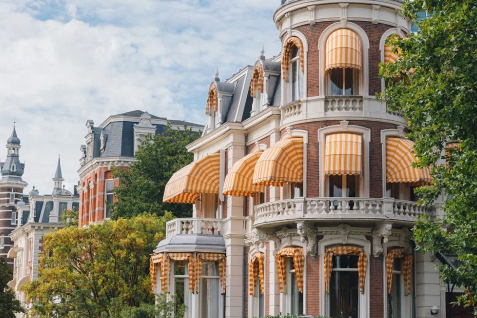 Ornate Amsterdam canal house with turret, yellow awnings, and flower boxes.