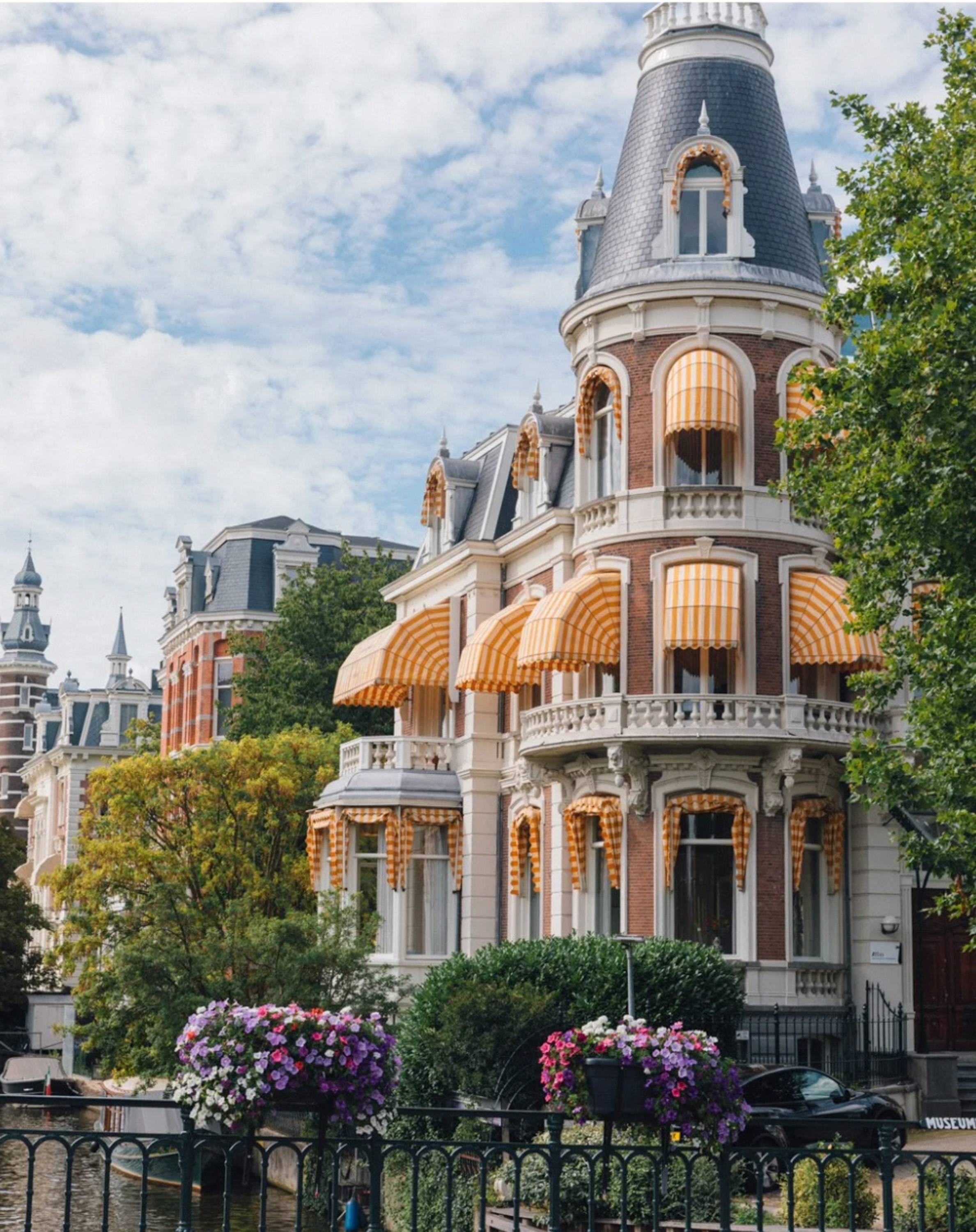 Ornate Amsterdam canal house with turret, yellow awnings, and flower boxes.