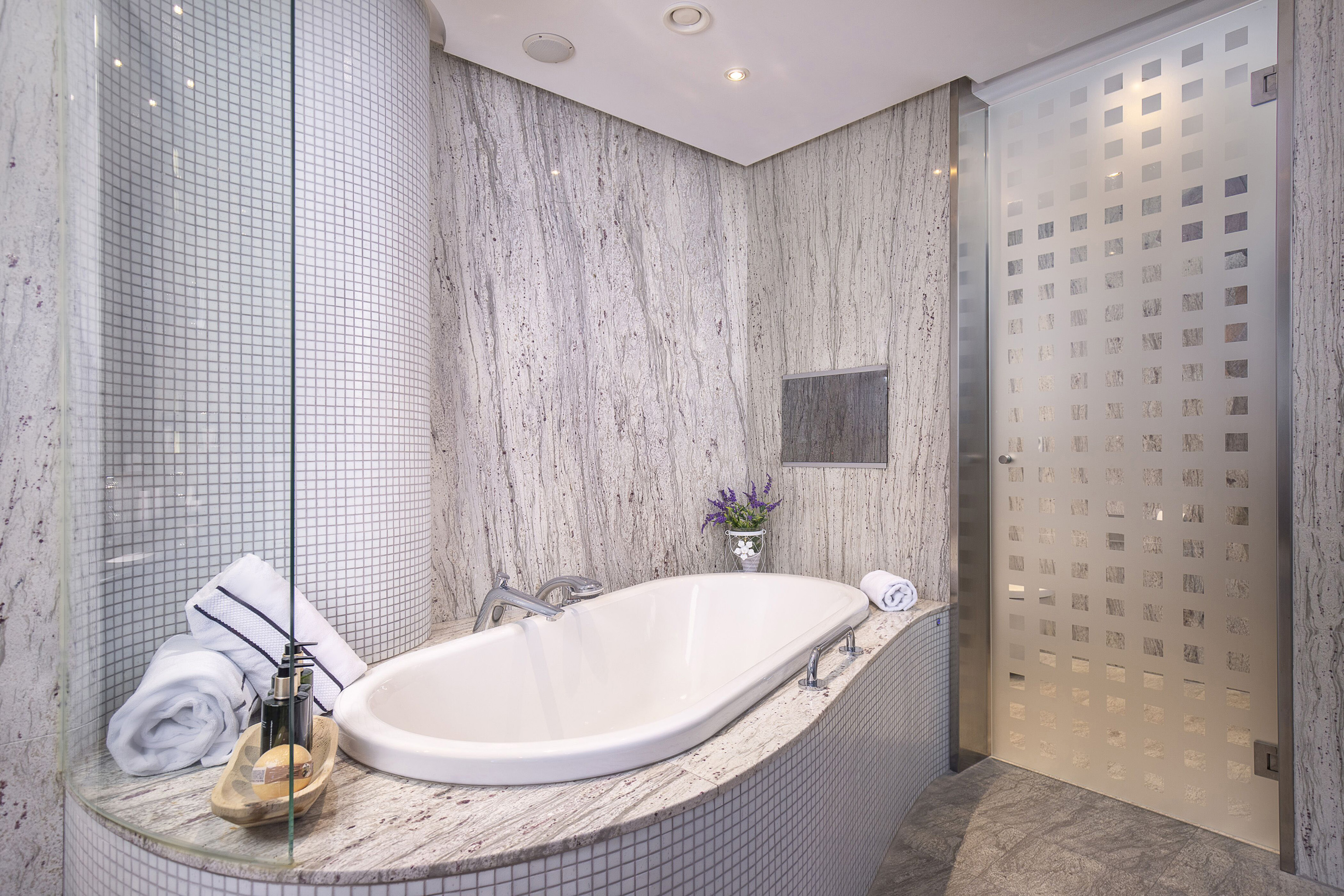 Modern bathroom with granite walls, white built-in tub, and mosaic tile surround.
