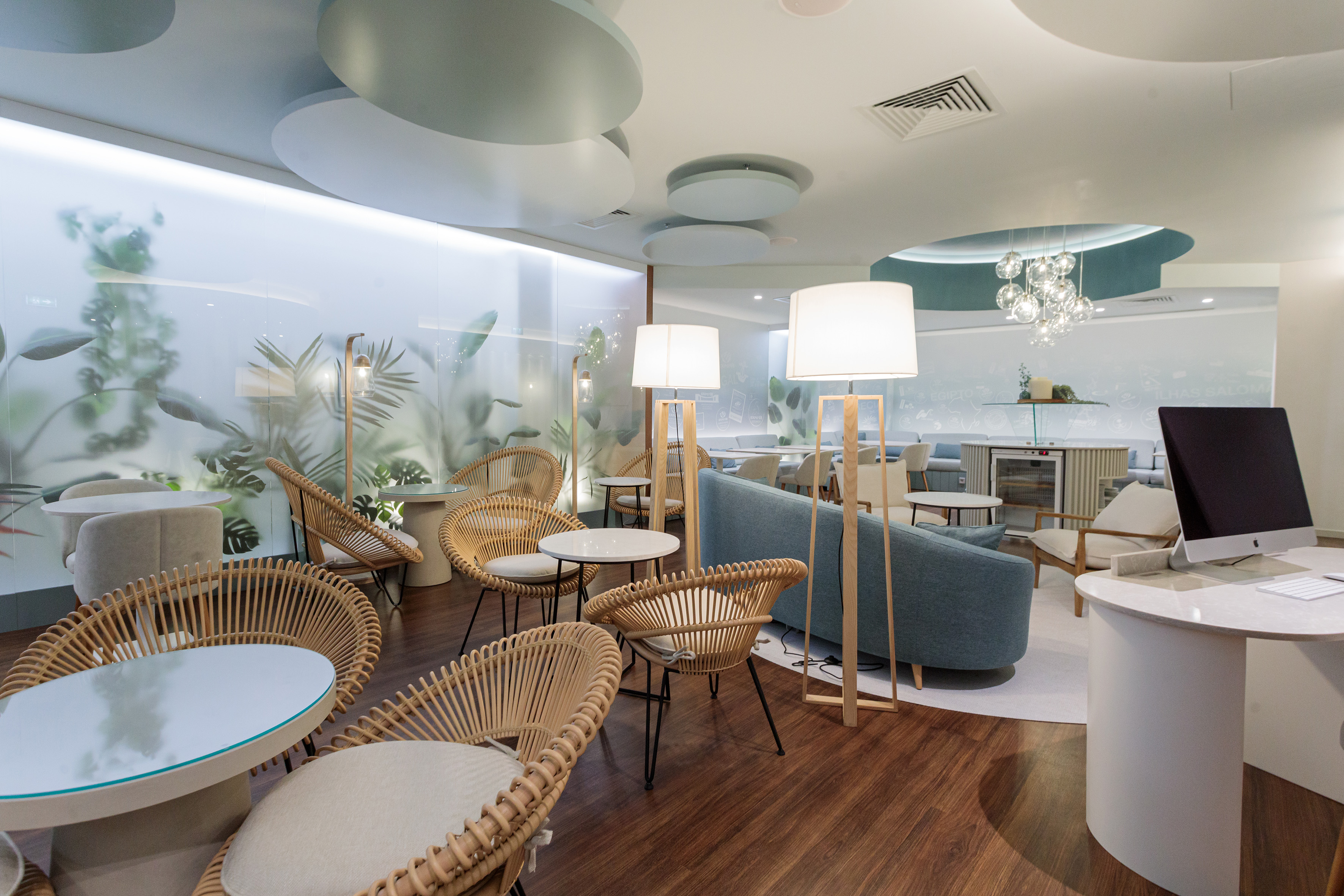 Modern lounge interior with rattan chairs, blue sofa, and frosted botanical wall.