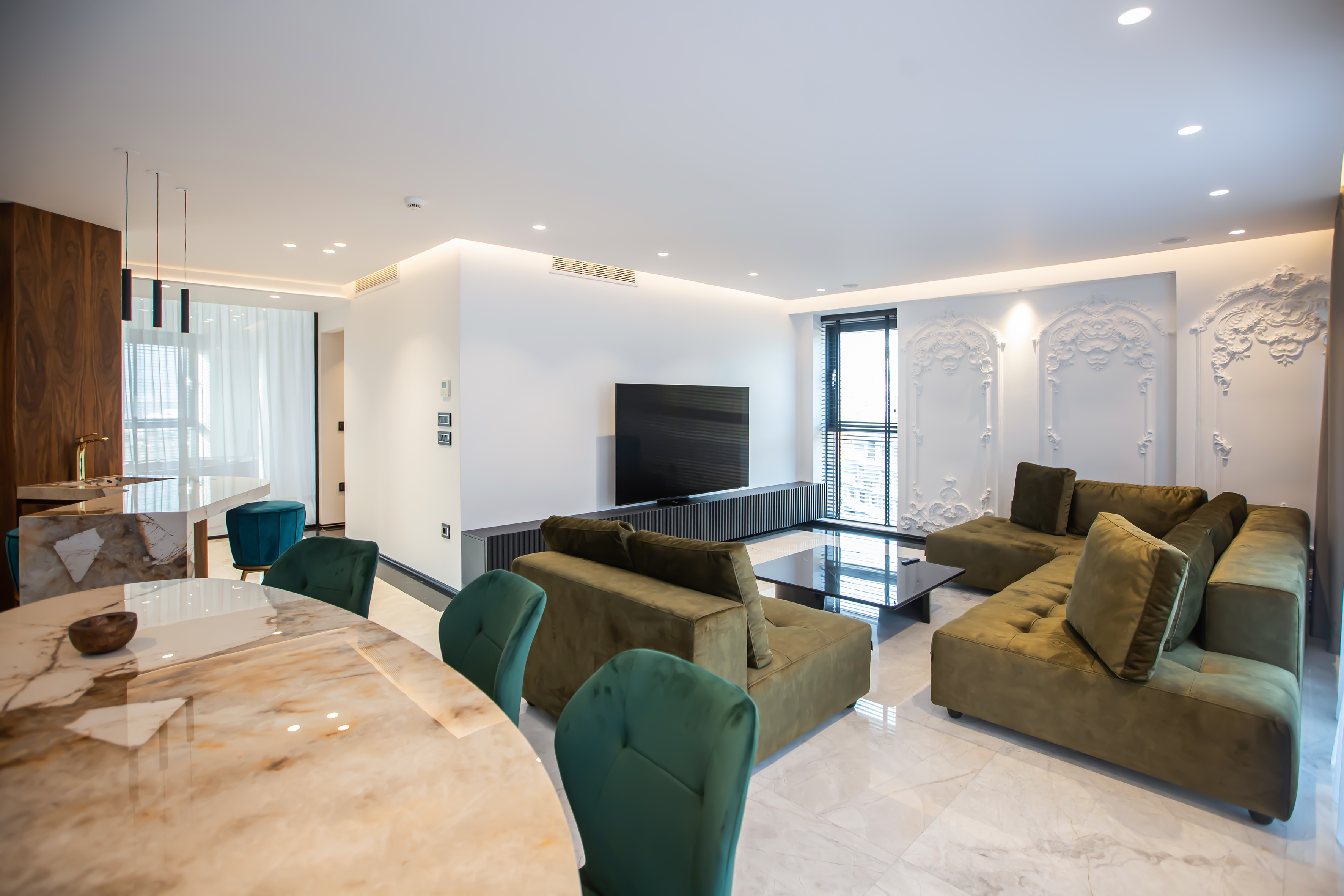 Modern living dining room with olive green sofa, marble table, and TV.