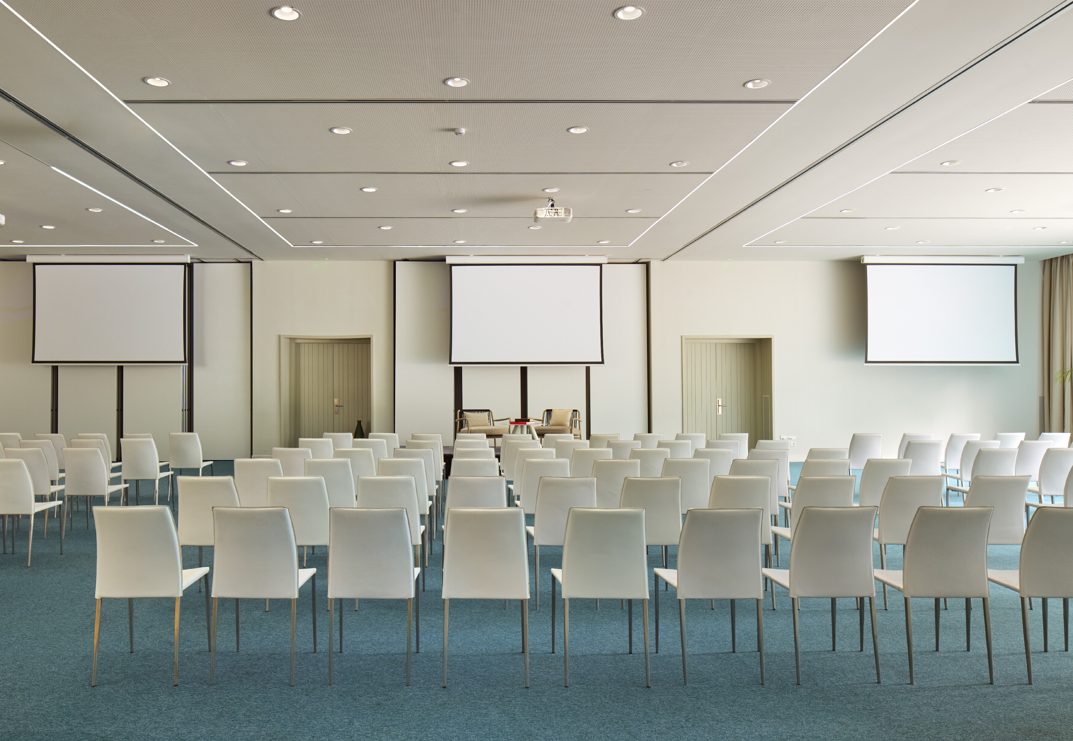 Empty modern conference room with white chairs and multiple projector screens.