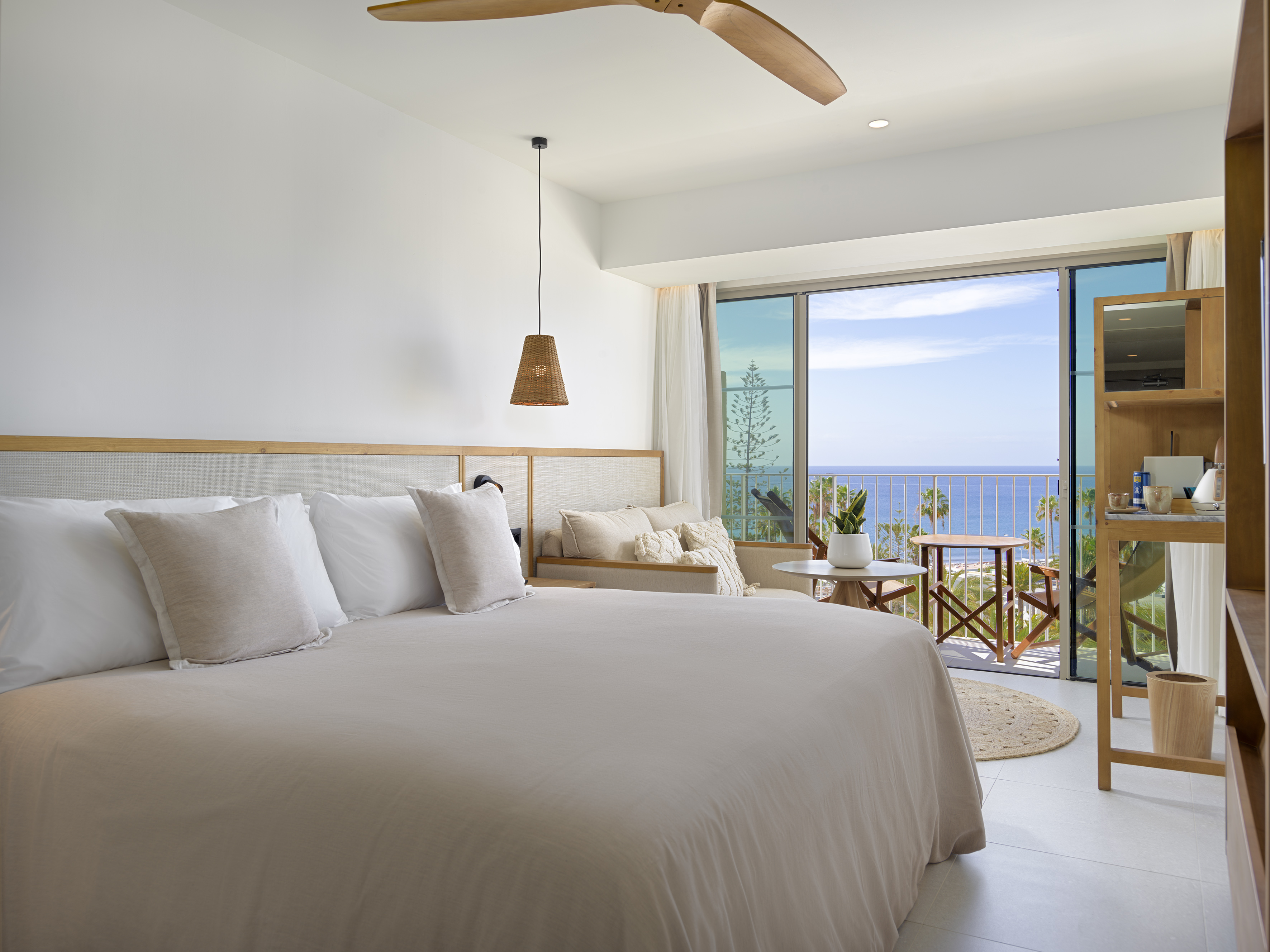 Bright ocean view hotel room with large bed and balcony.
