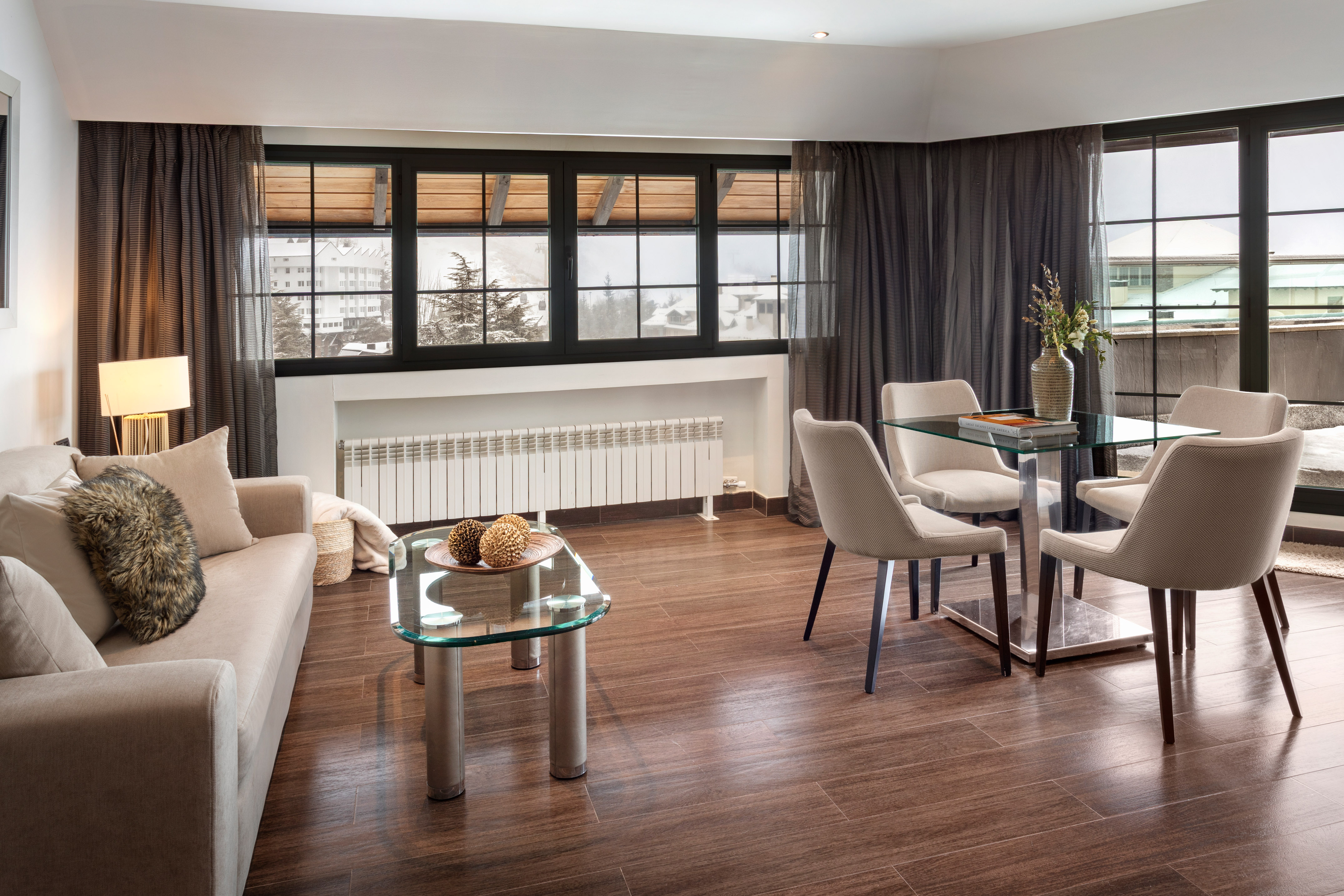 Modern living room, dining area, beige sofa, glass tables, snowy mountain view.