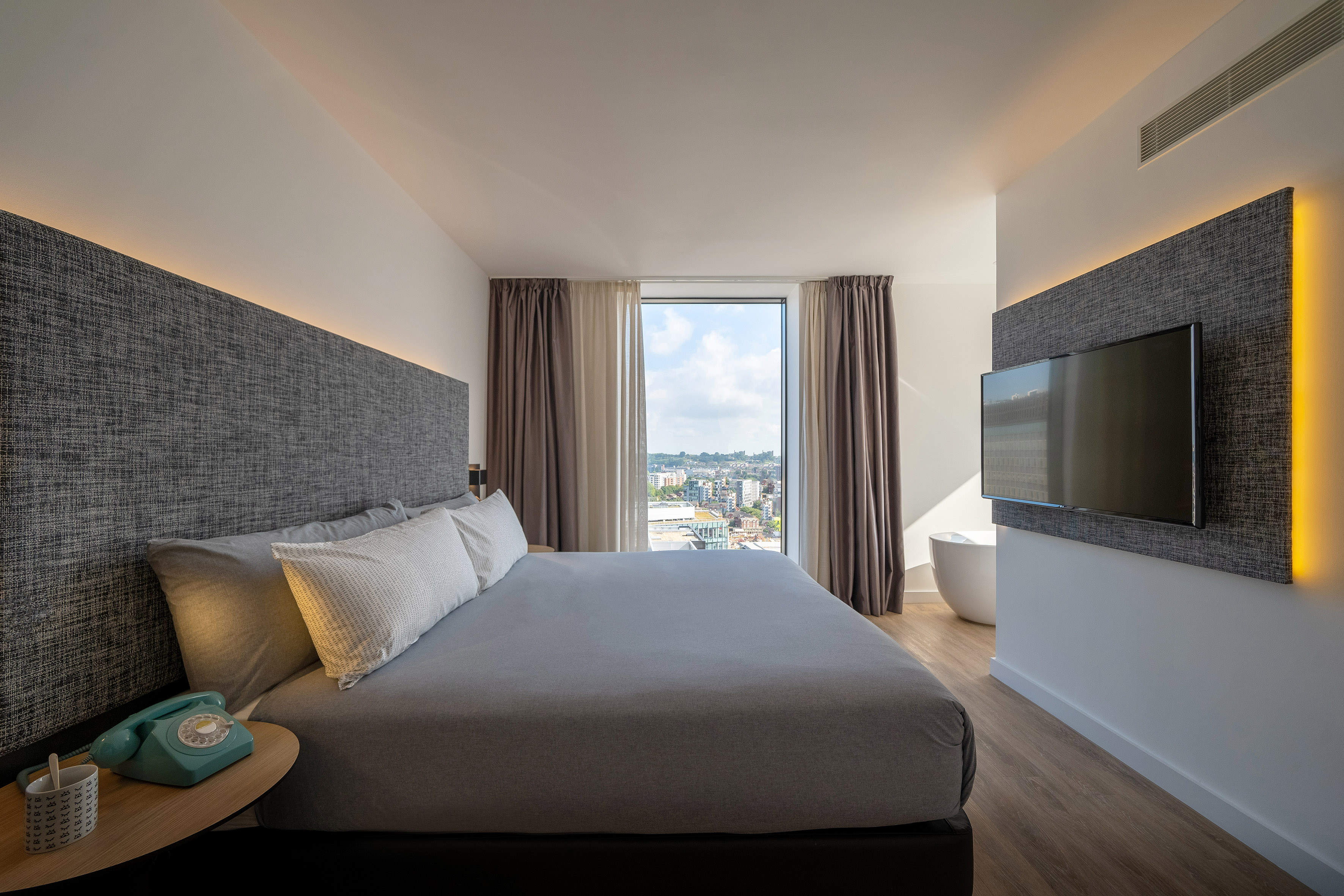 Modern hotel room with large bed, city view, and mood lighting.