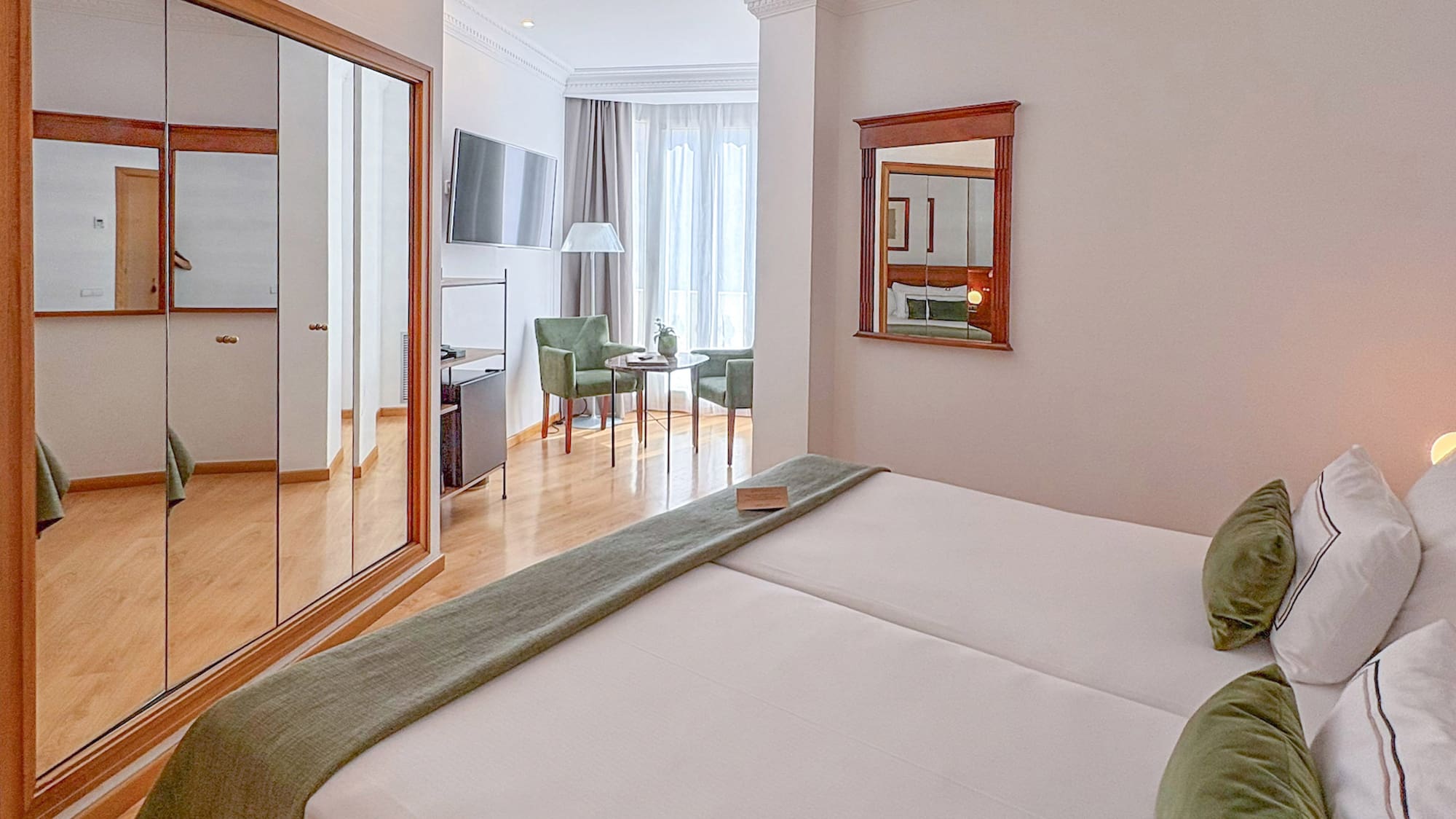 Comfortable hotel room with two beds, green accents, mirrored wardrobe, and seating area.
