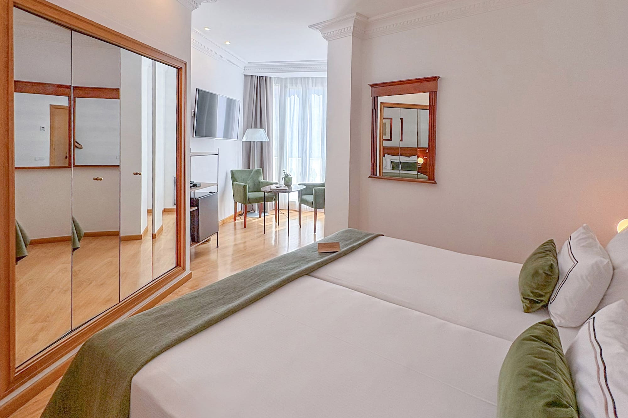 Comfortable hotel room with two beds, green accents, mirrored wardrobe, and seating area.