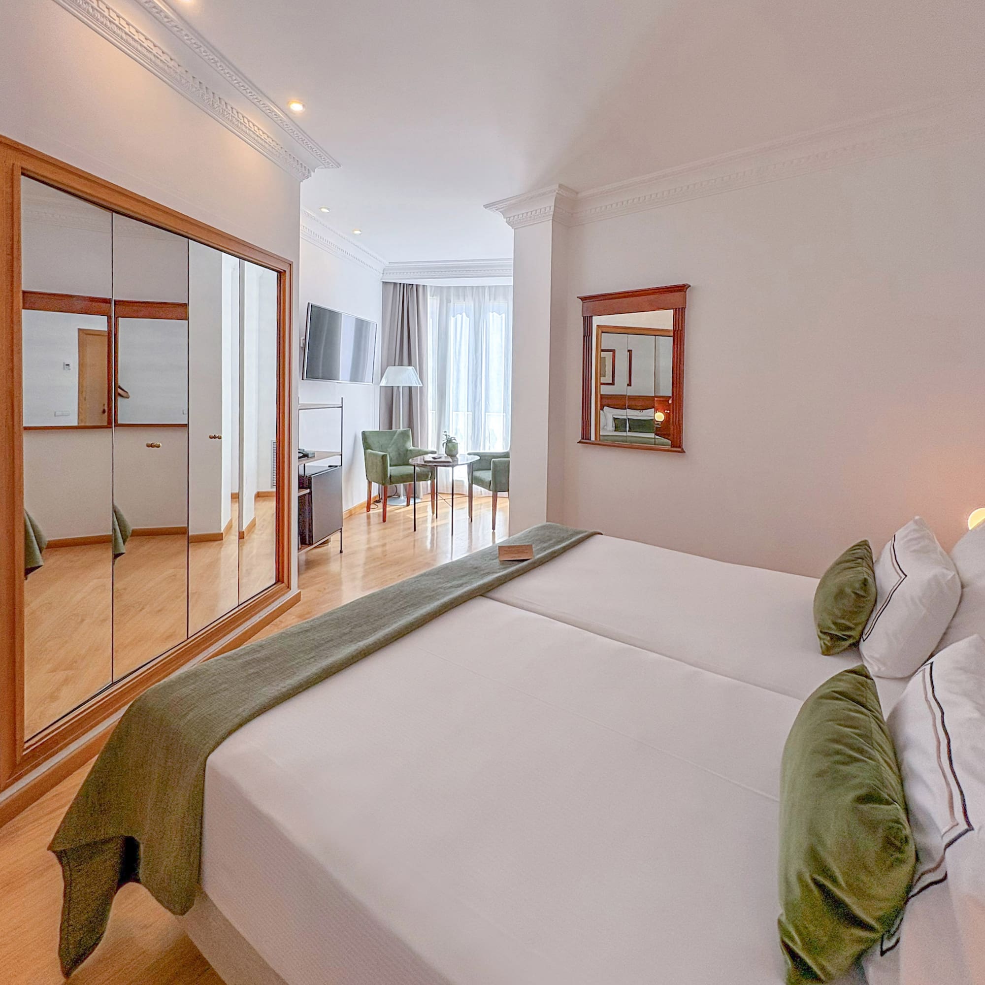 Comfortable hotel room with two beds, green accents, mirrored wardrobe, and seating area.
