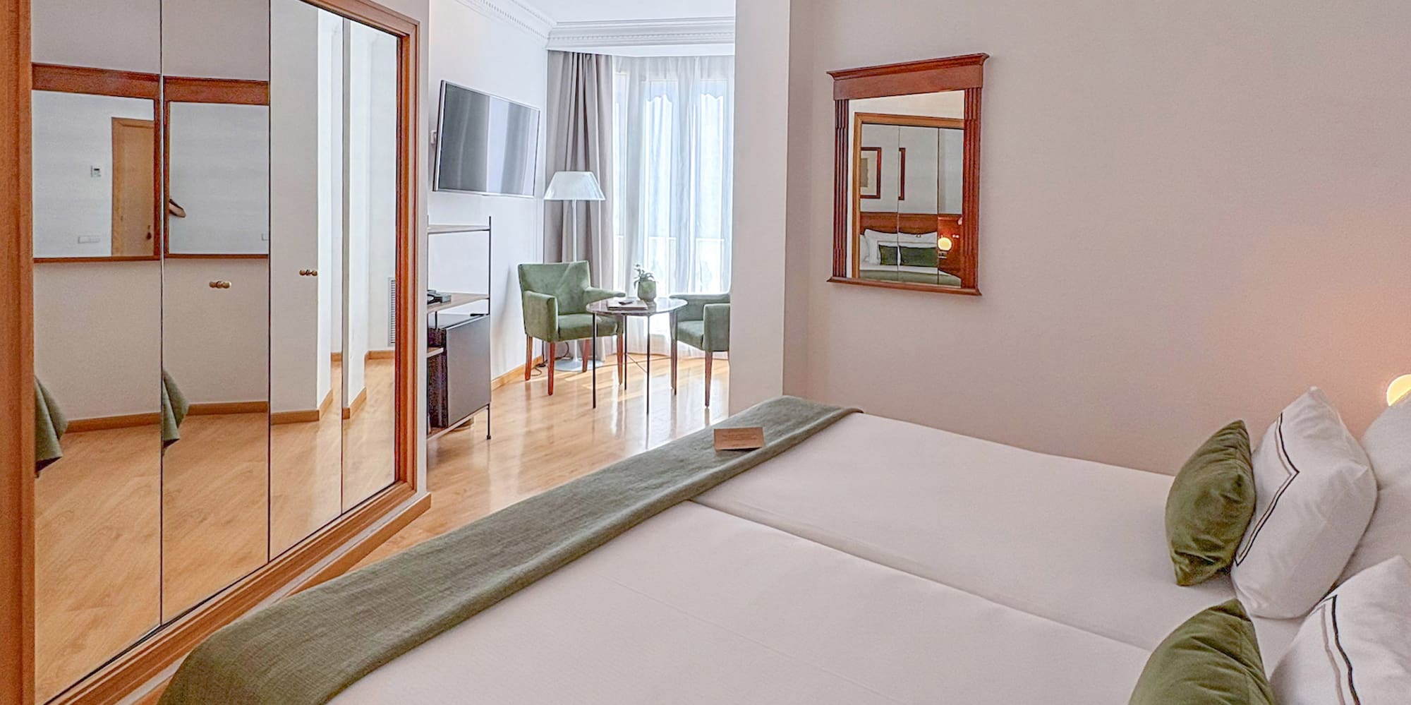 Comfortable hotel room with two beds, green accents, mirrored wardrobe, and seating area.