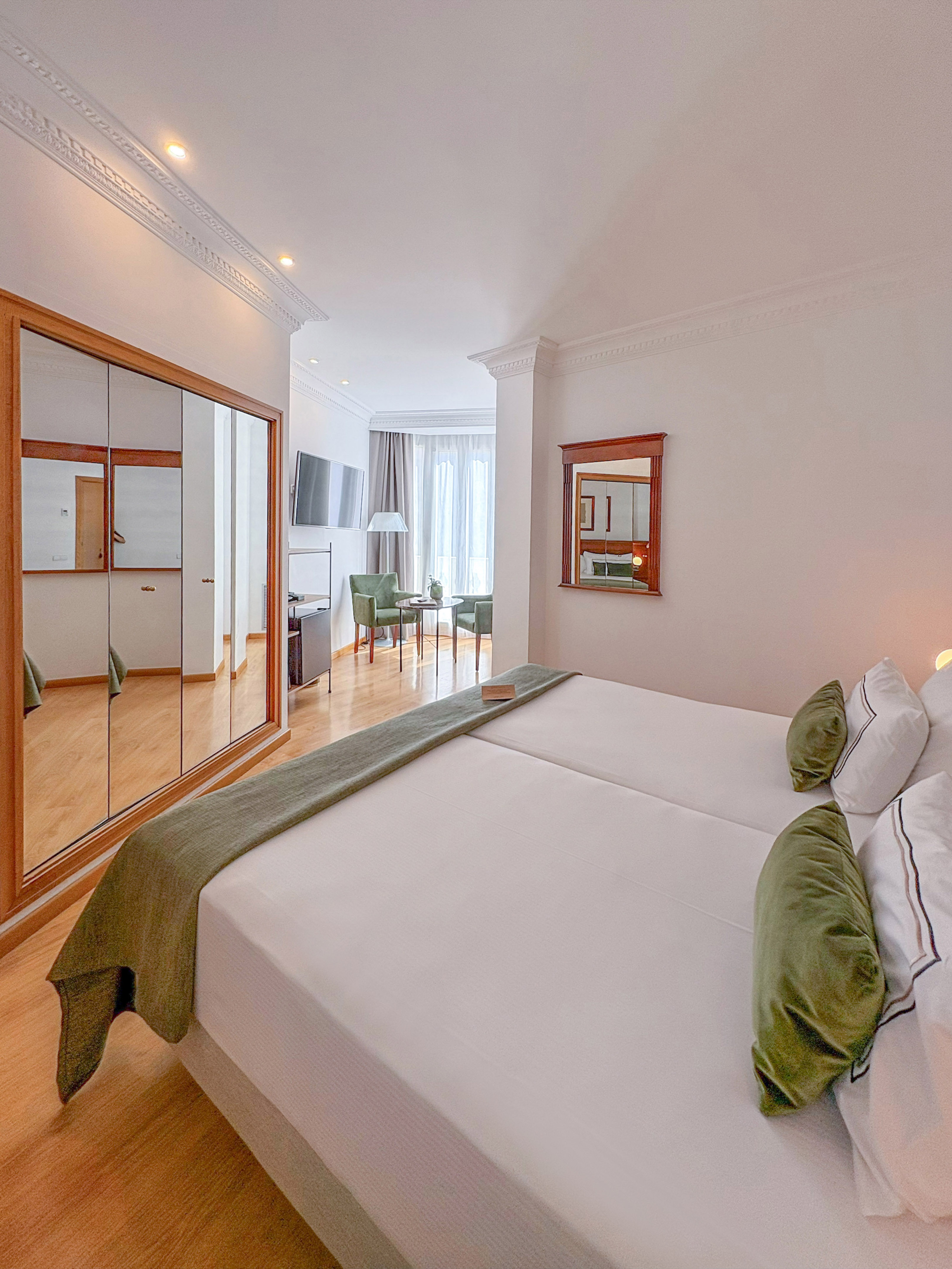 Comfortable hotel room with two beds, green accents, mirrored wardrobe, and seating area.