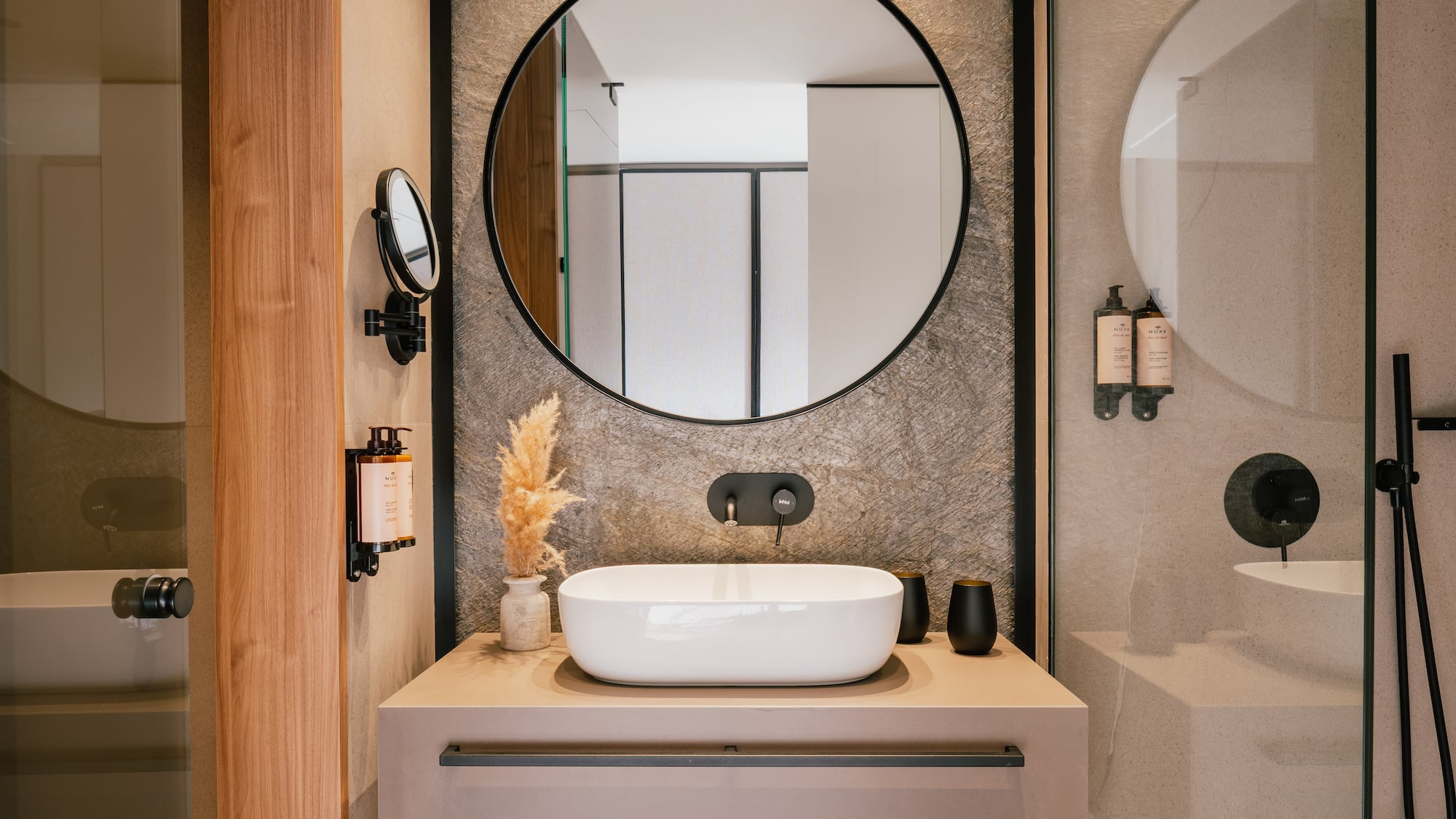 Sleek bathroom vanity, round mirror, white vessel sink, black faucet, stone wall.