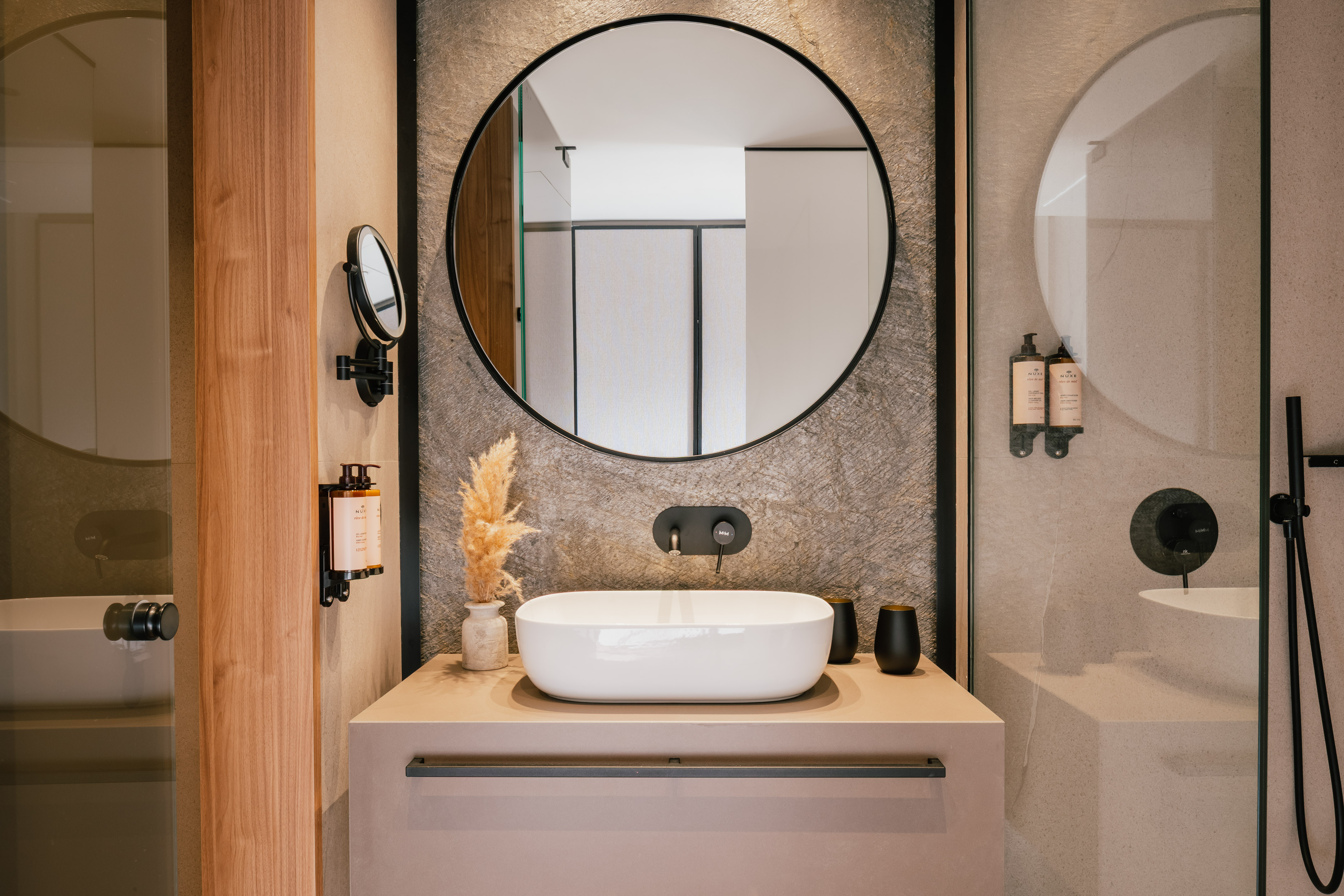 Sleek bathroom vanity, round mirror, white vessel sink, black faucet, stone wall.