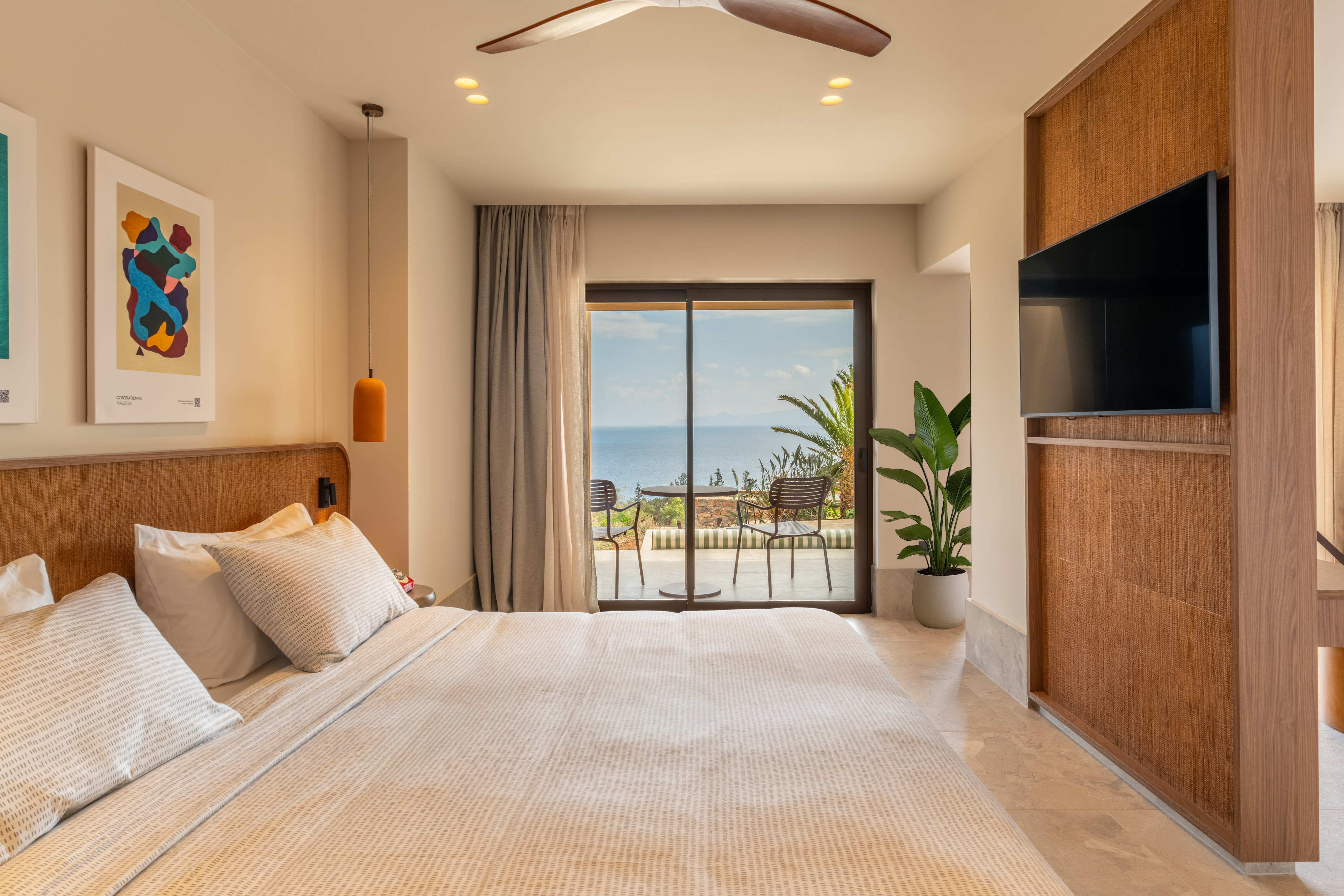 Modern resort bedroom with ocean view balcony, large bed, and rattan decor.
