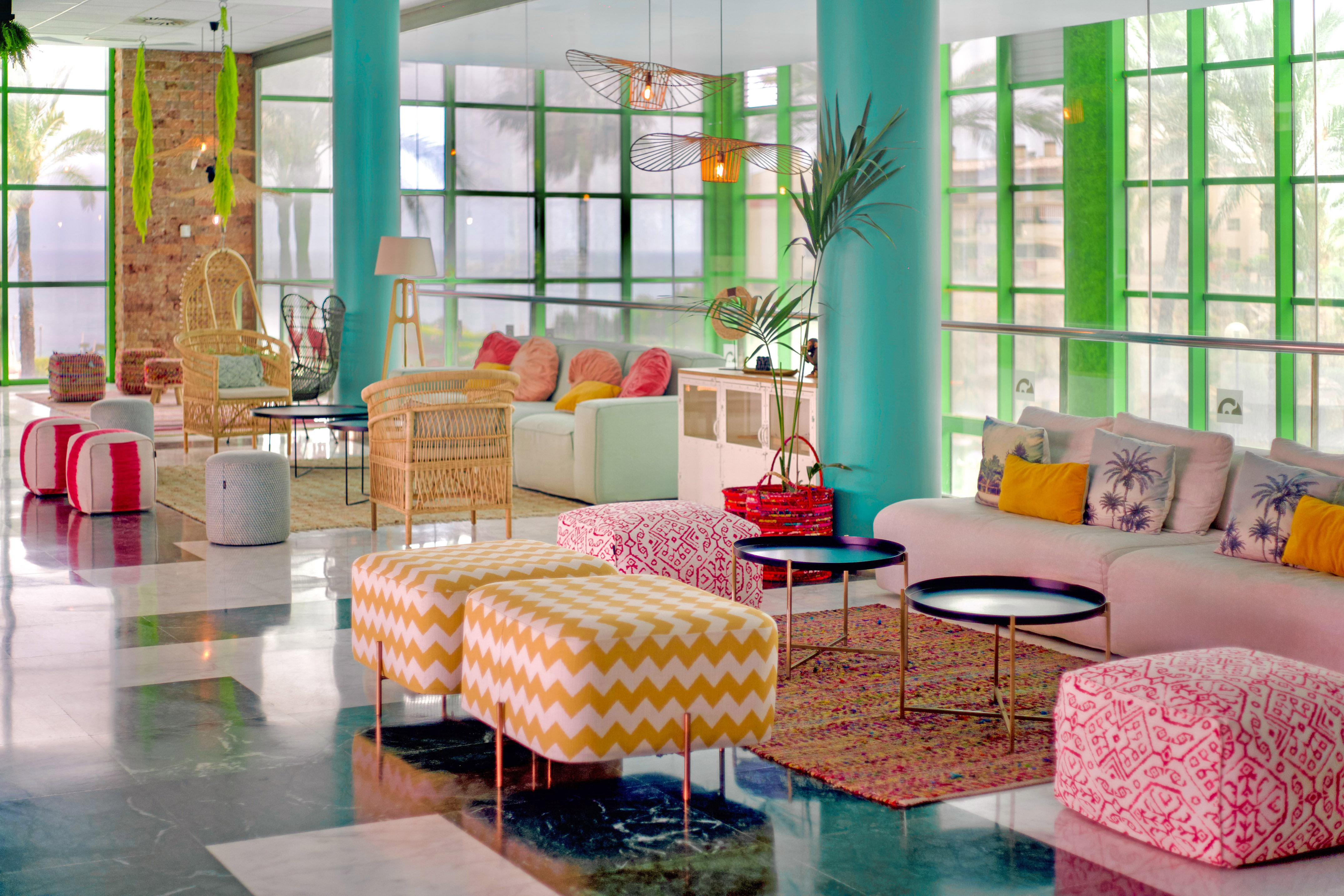 Vibrant hotel lobby with colorful seating, wicker chairs, and palm tree views.