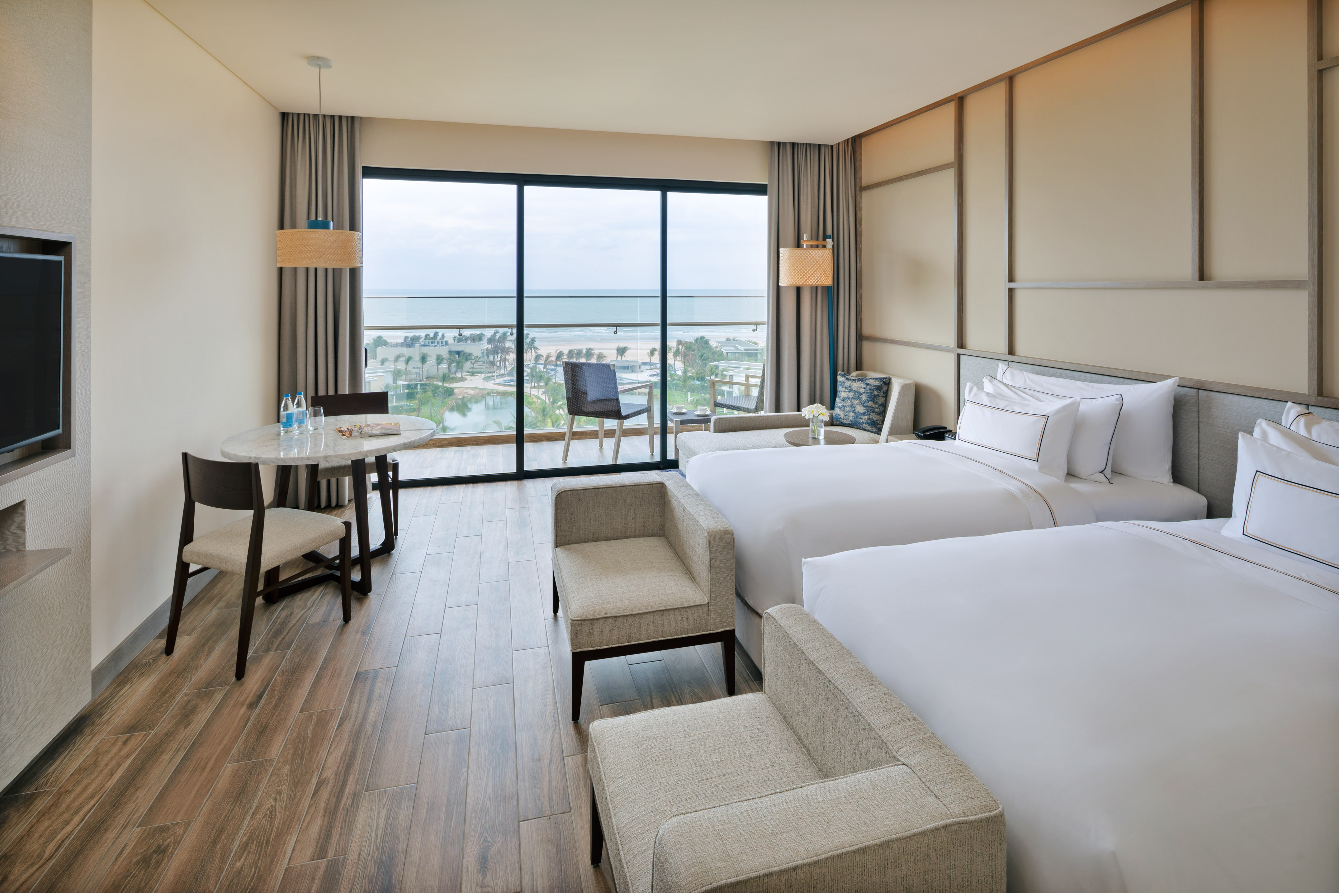 Spacious hotel room with twin beds, ocean view balcony, and wood floor.
