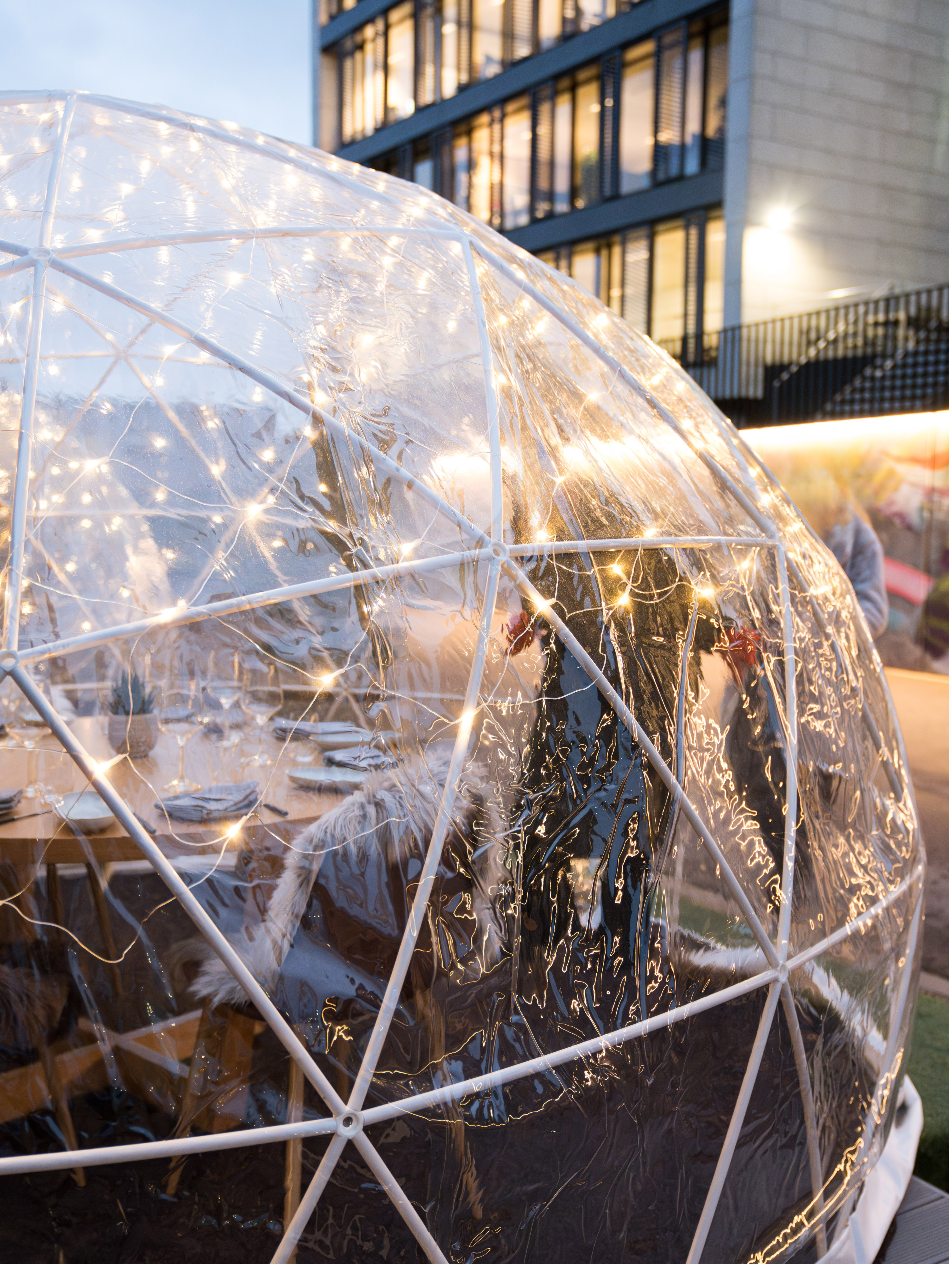 Illuminated dining igloo with set table and furry seats for outdoor dining.