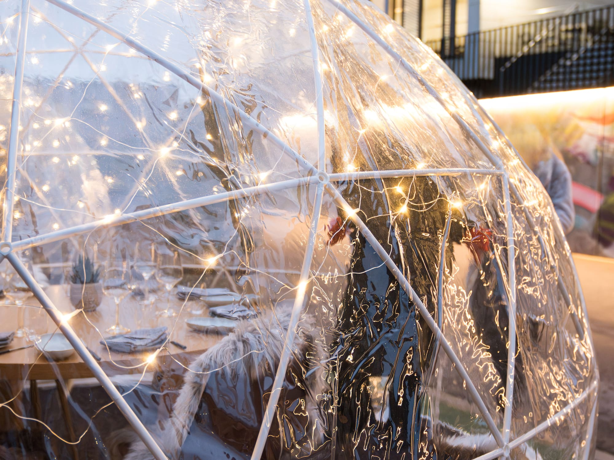 Illuminated dining igloo with set table and furry seats for outdoor dining.