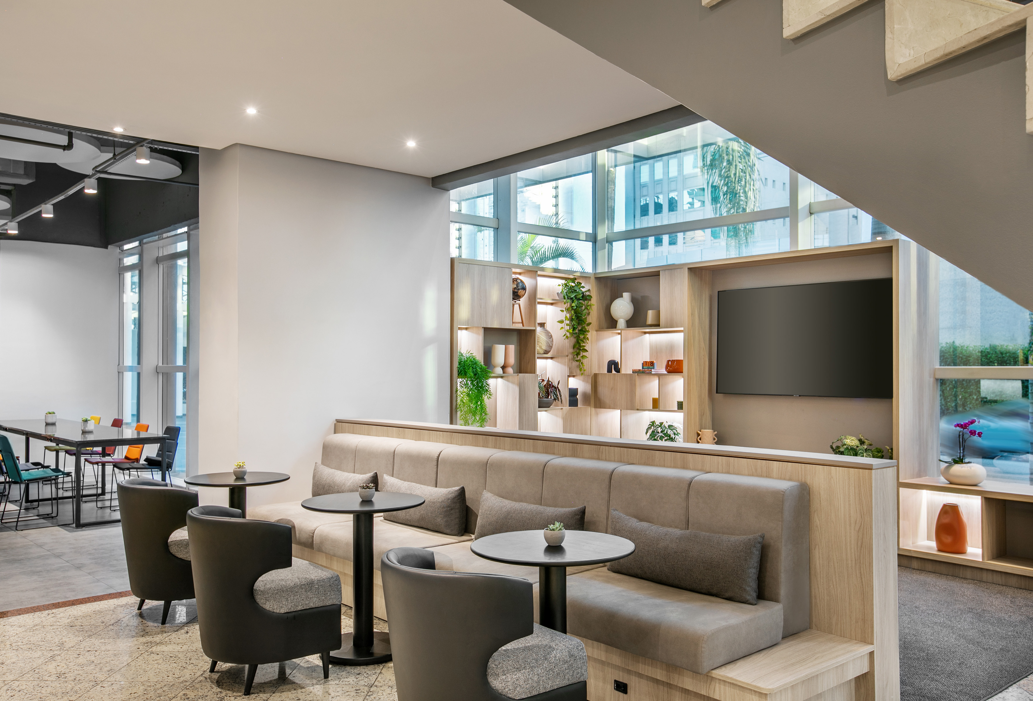 Modern lounge with neutral seating, wood decor, plants, and large windows.