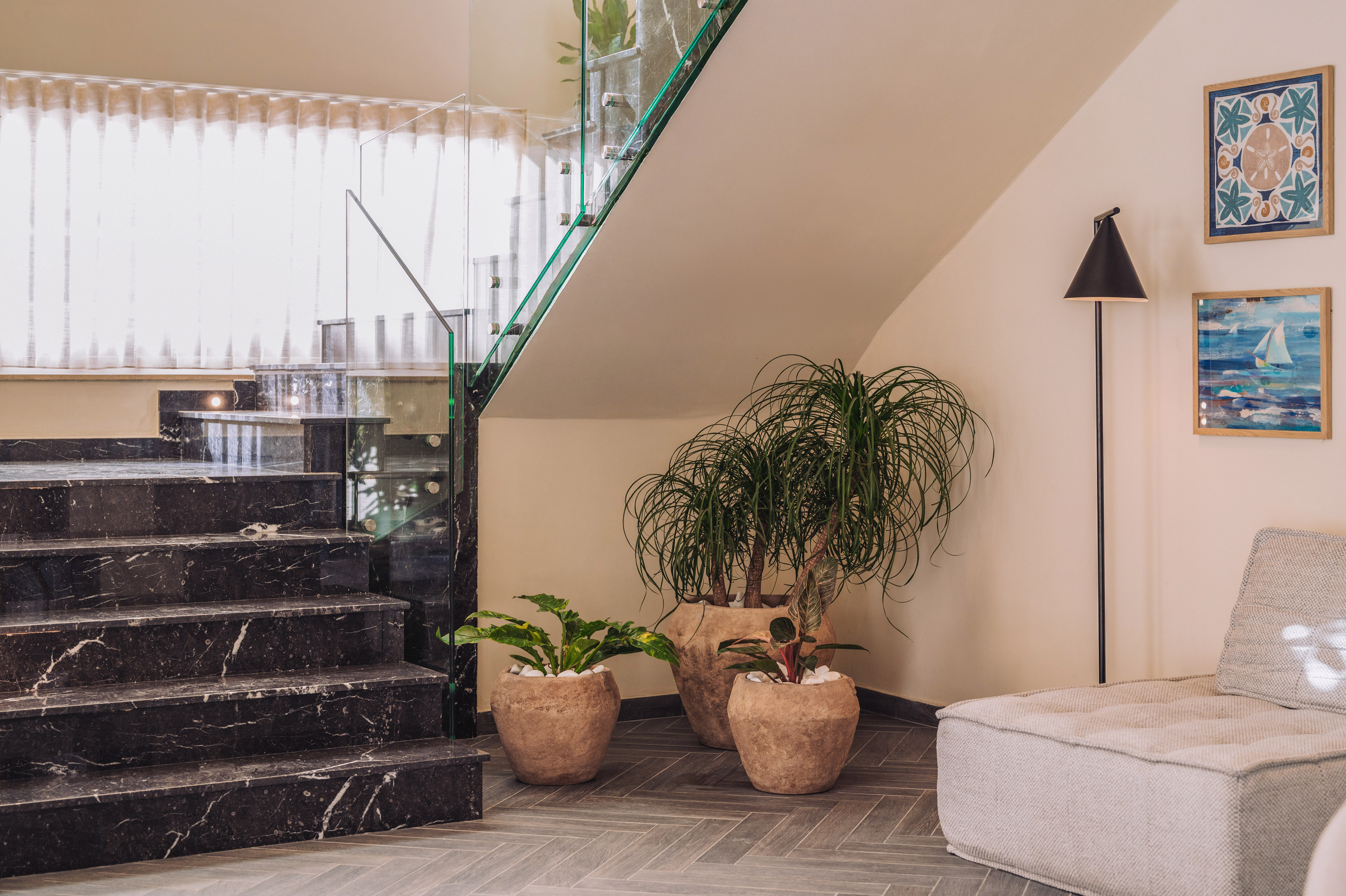 Black marble stairs, glass railing, tropical plants, and modern lounge interior.