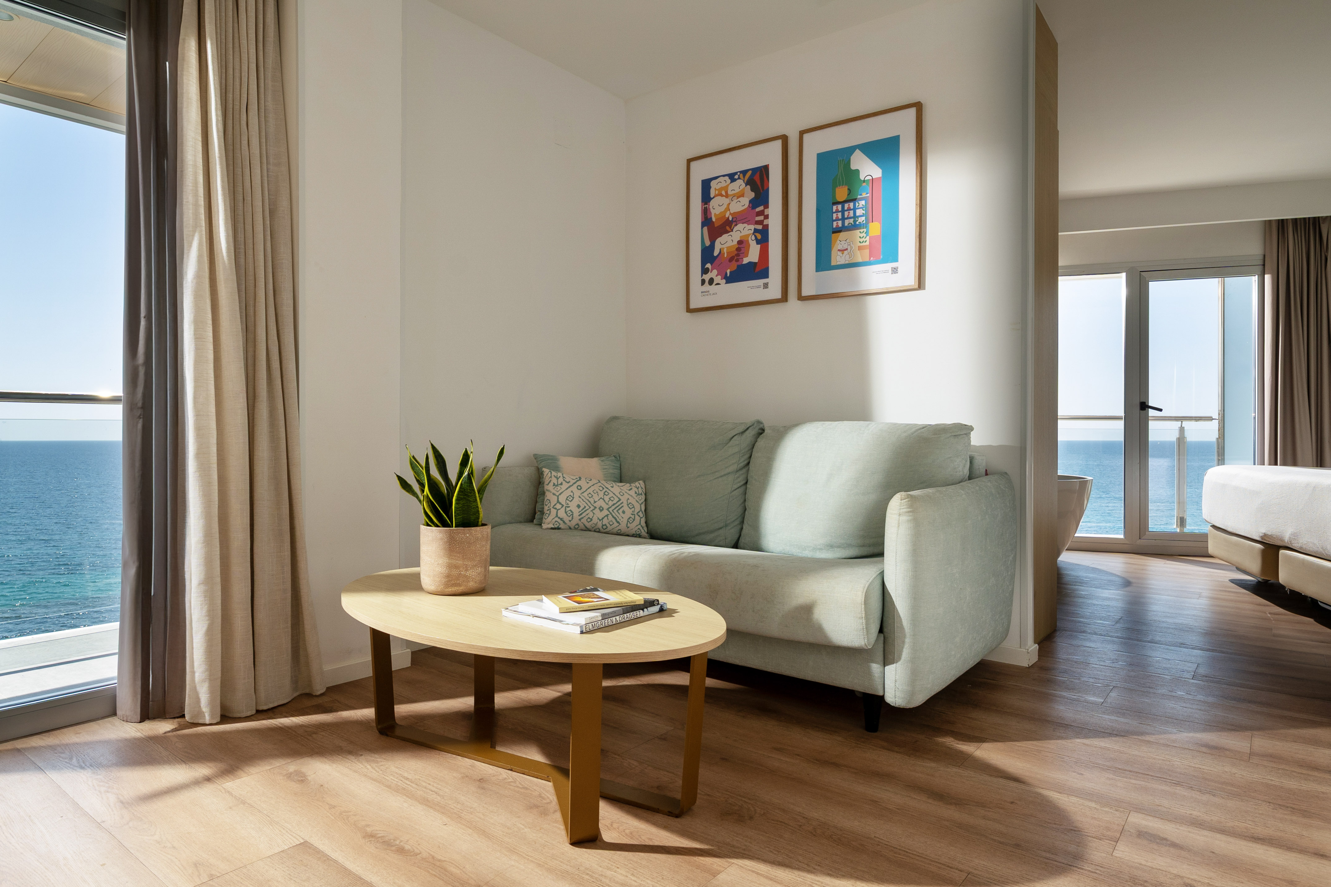 Modern hotel suite living area with ocean view, mint sofa, and wooden coffee table.