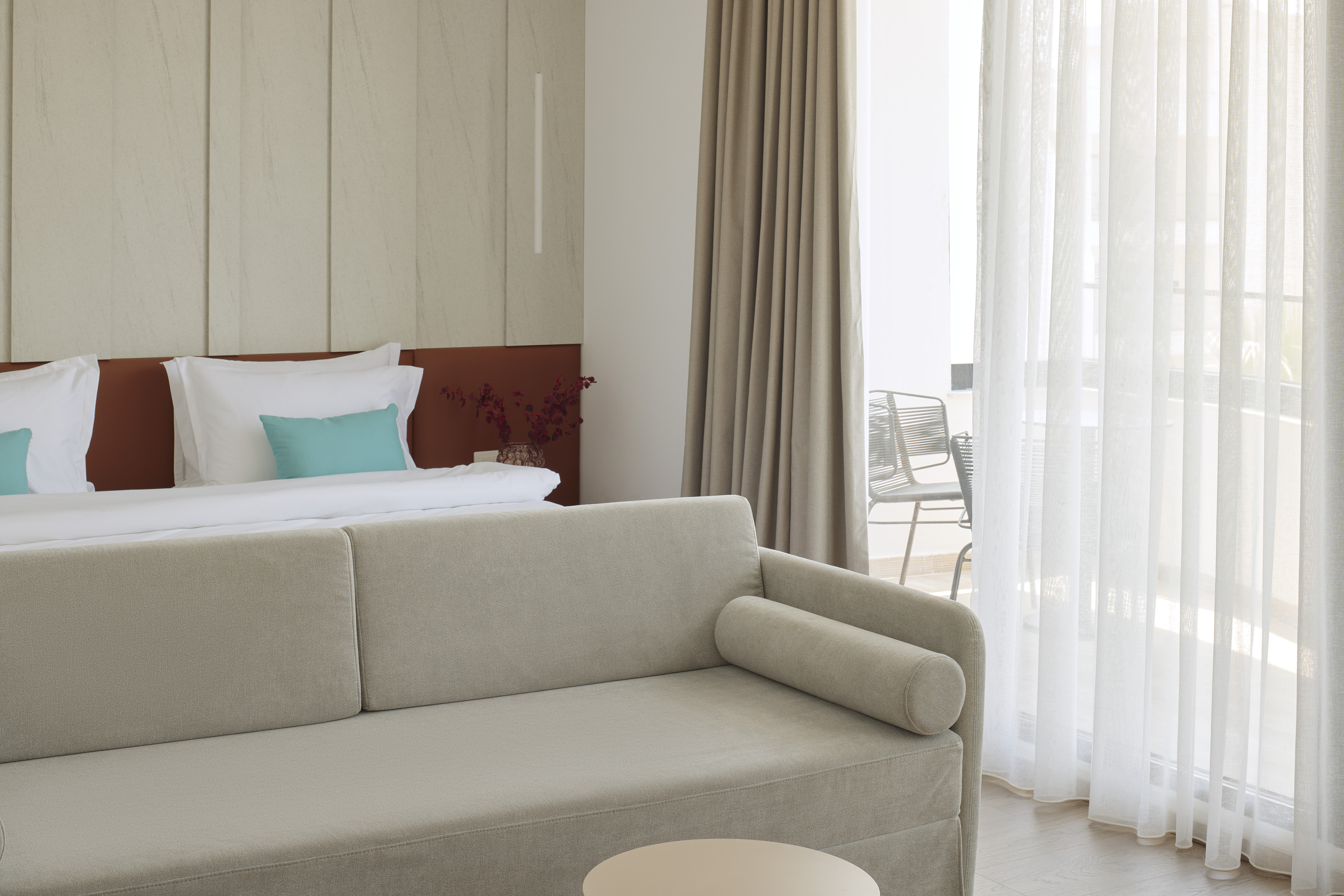 Hotel room interior with beige sofa, bed, and balcony access.
