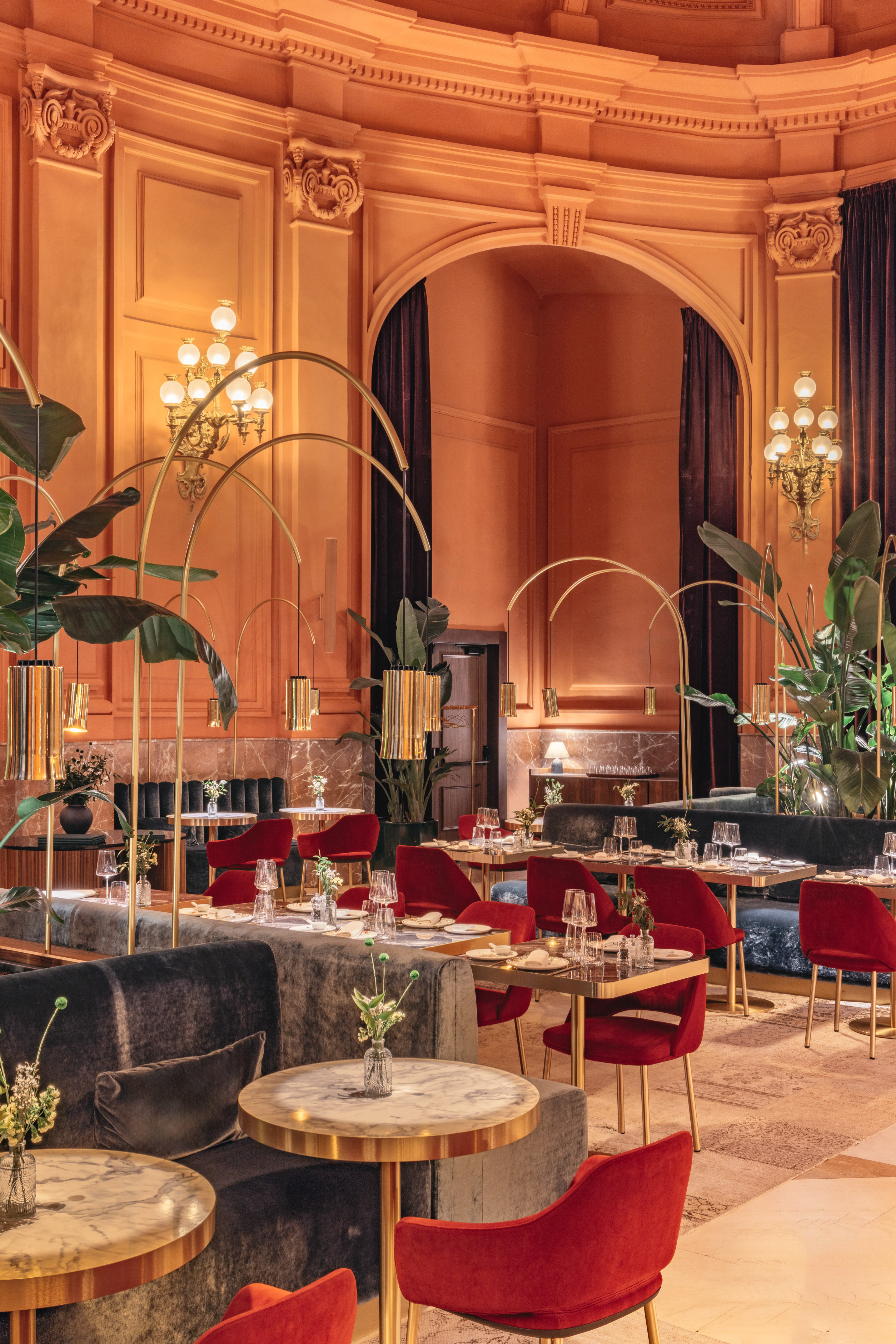Luxury restaurant dining room with ornate orange walls, red chairs, gold decor.