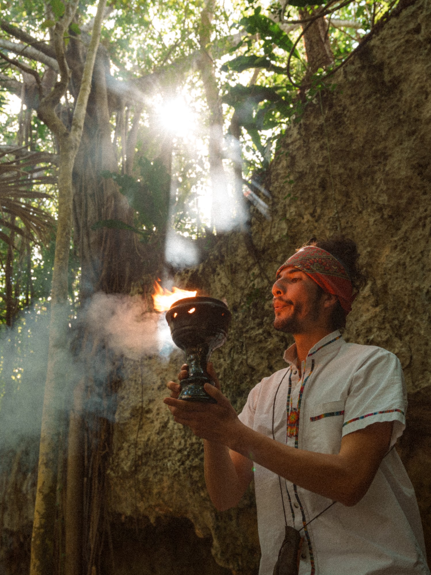 a man holding a fire bowl in front of a rock wall