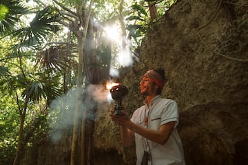 a man holding a fire bowl in front of a rock wall