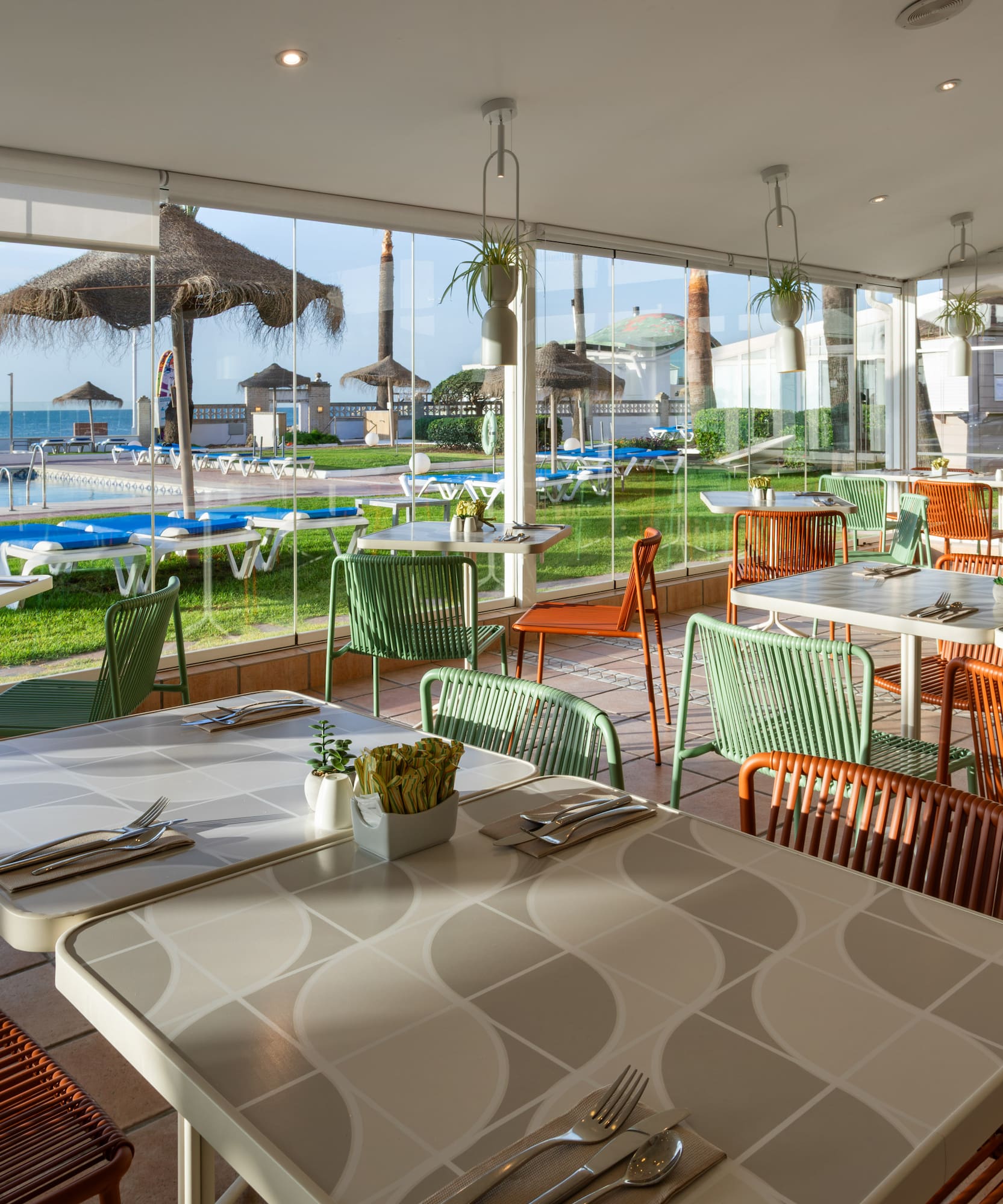 Modern dining room with pool and sea views. Colorful green & orange chairs.