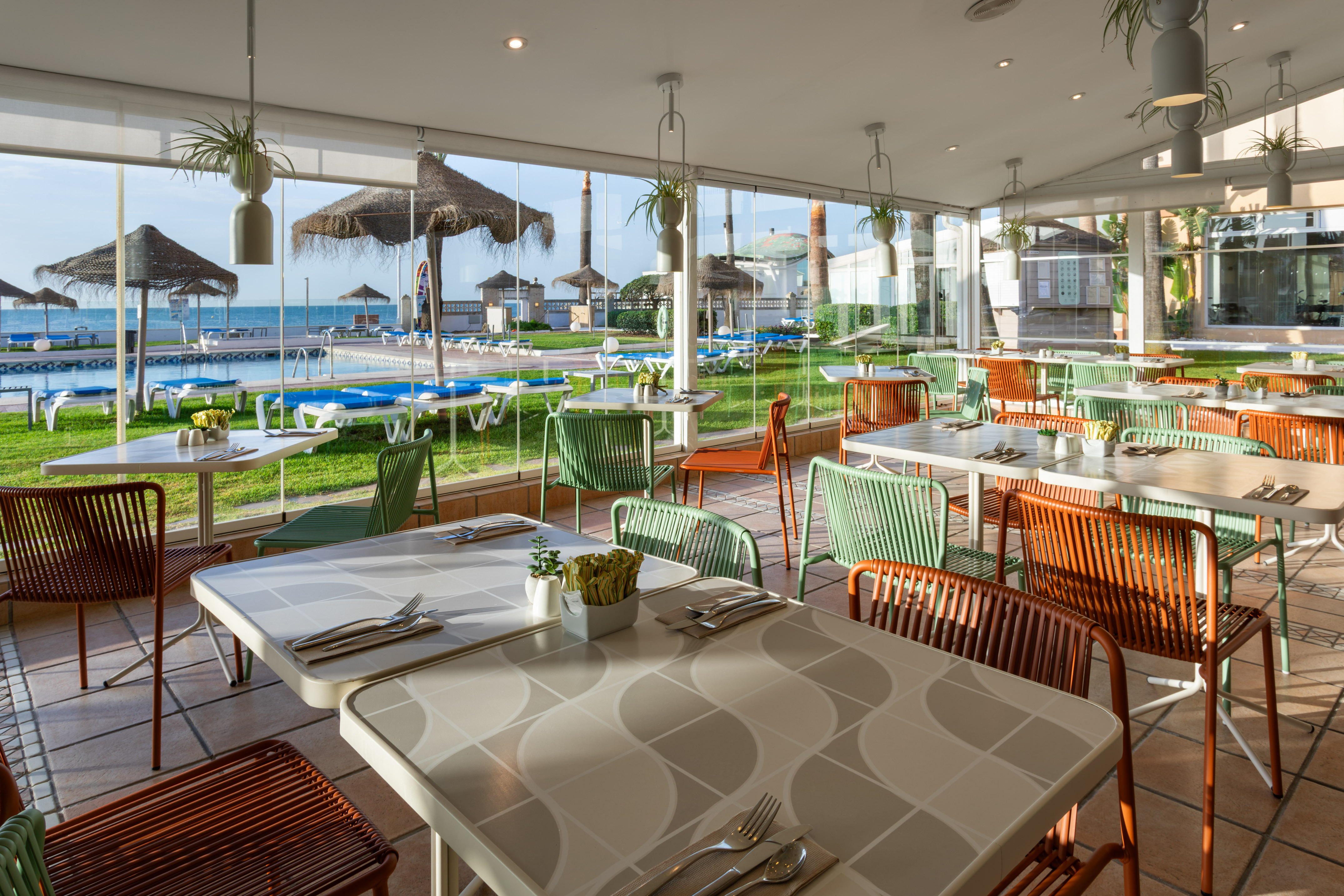 Modern dining room with pool and sea views. Colorful green & orange chairs.