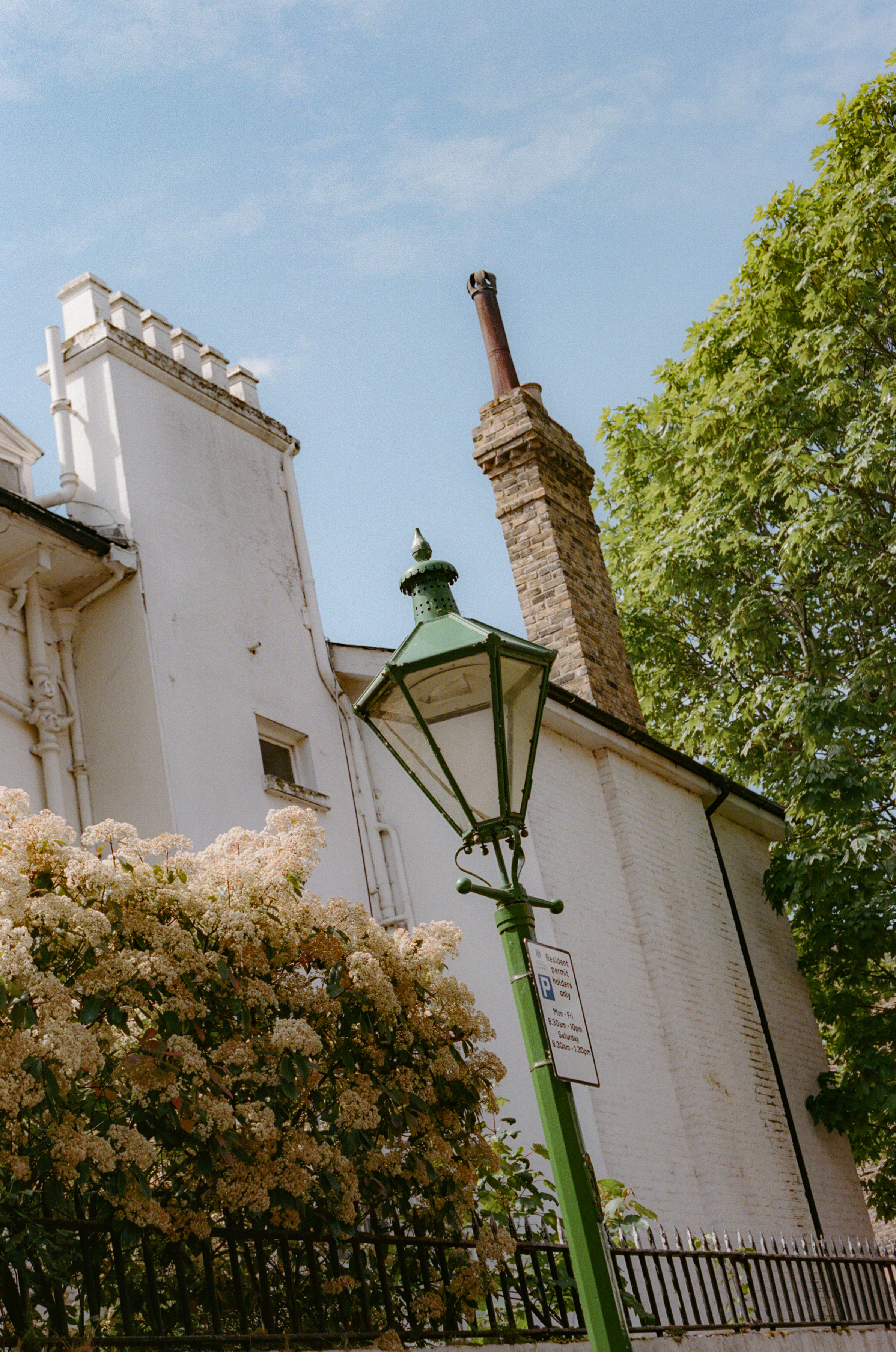 Ornate green lamp post, white building, brick chimney, green trees, blue sky.