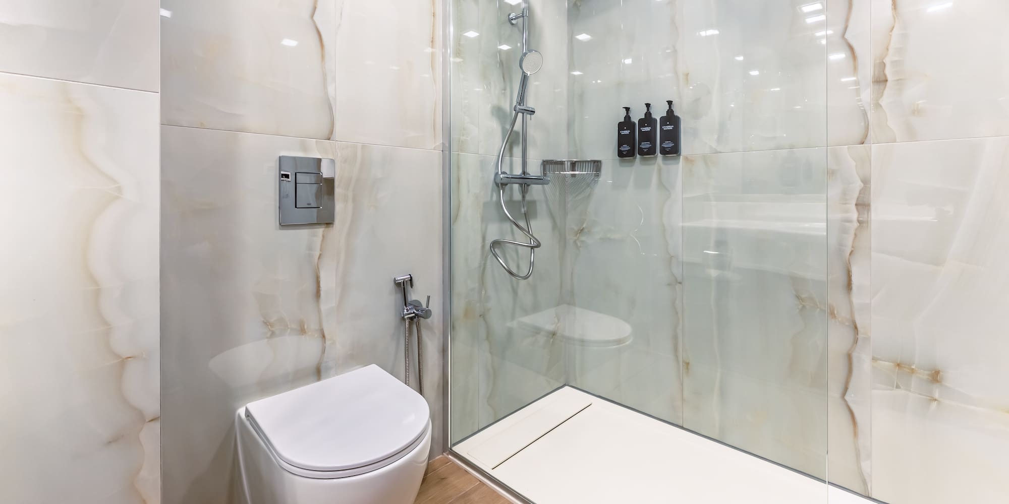 Modern bathroom with toilet, walk-in shower, and white marble-look tiles.
