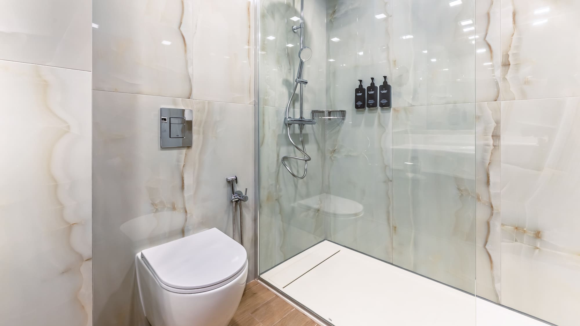 Modern bathroom with toilet, walk-in shower, and white marble-look tiles.