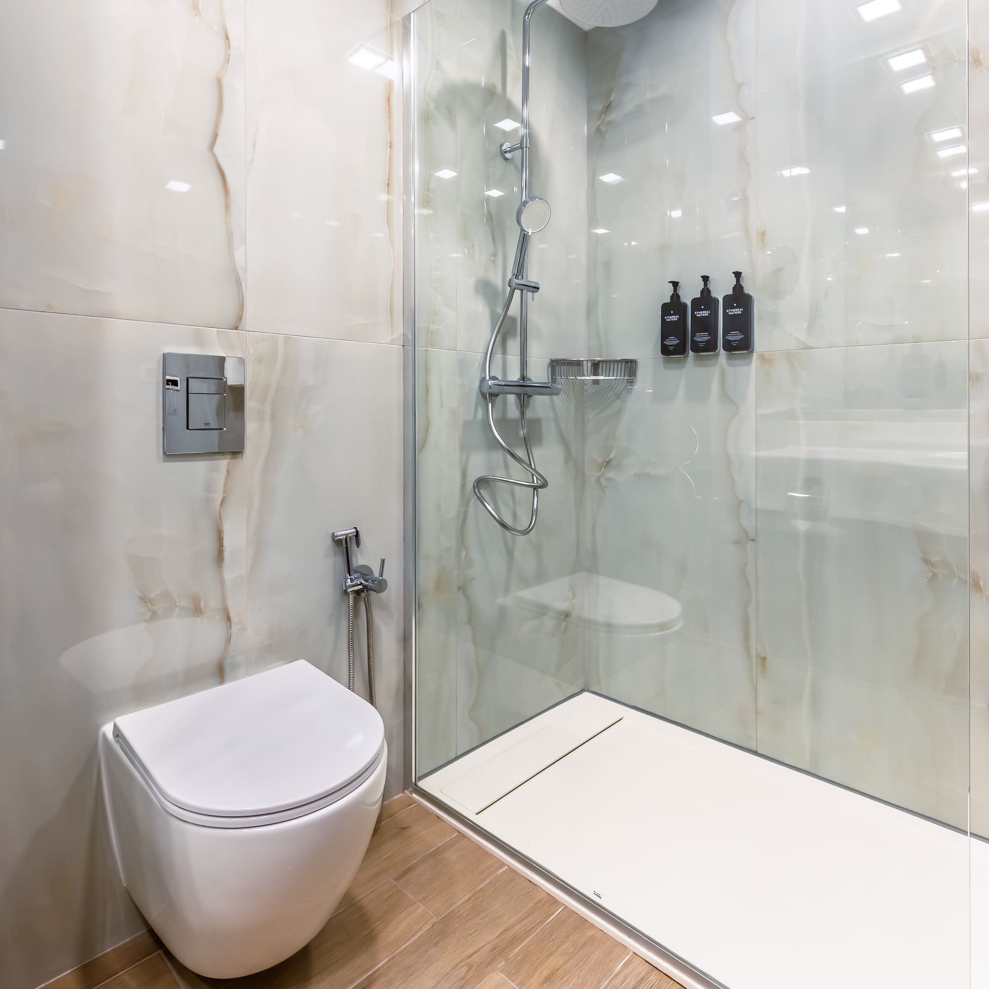 Modern bathroom with toilet, walk-in shower, and white marble-look tiles.