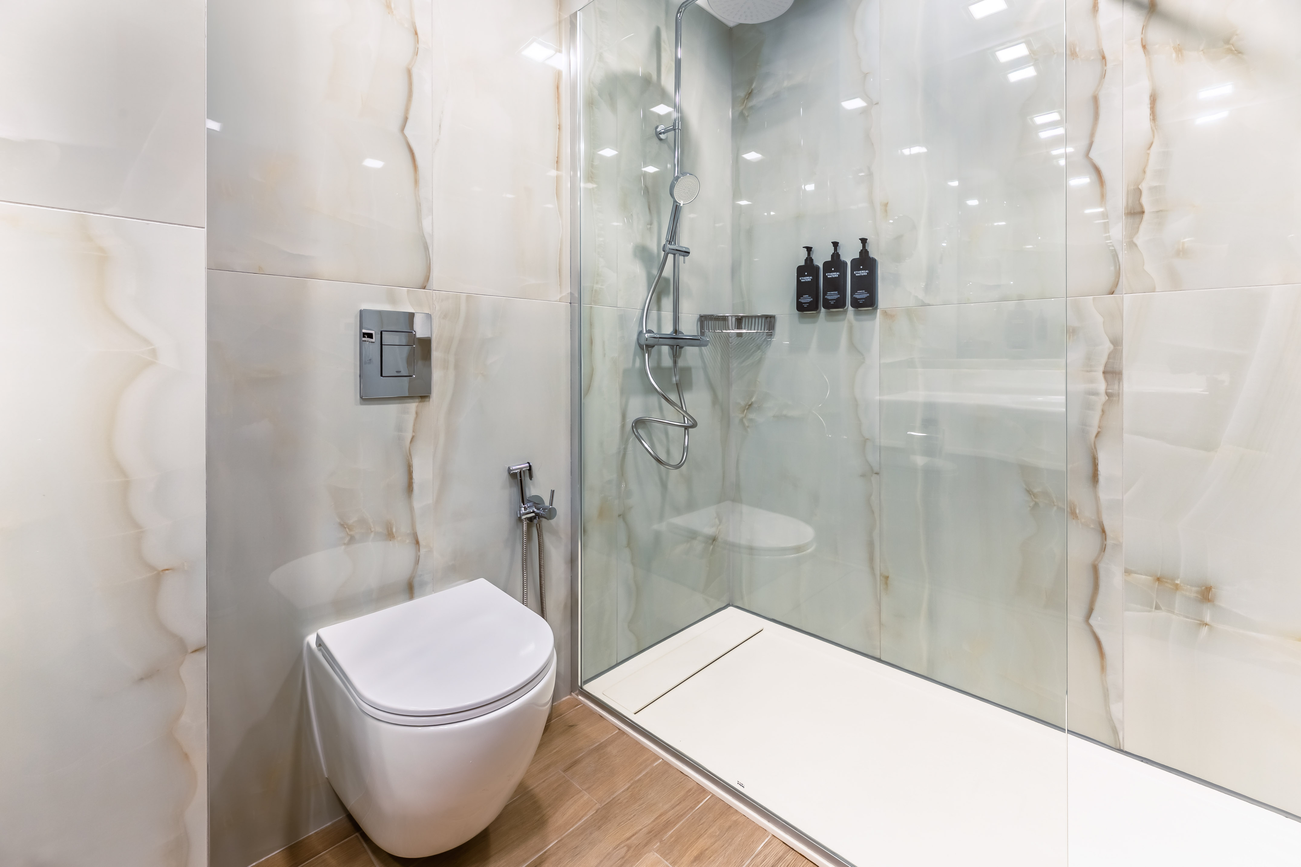 Modern bathroom with toilet, walk-in shower, and white marble-look tiles.