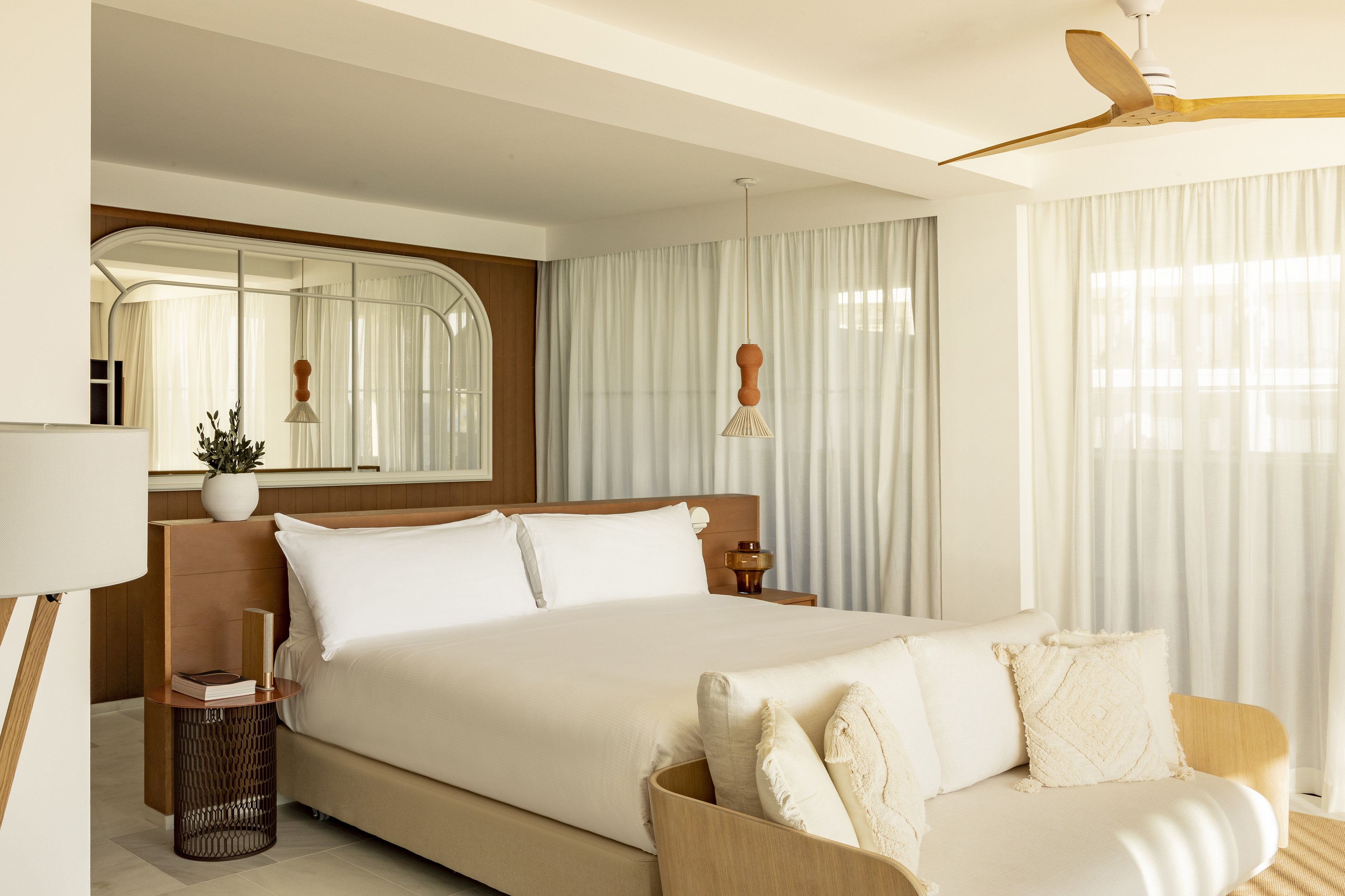 Bright, modern bedroom with white bed, wood accents, sheer curtains, and ceiling fan.