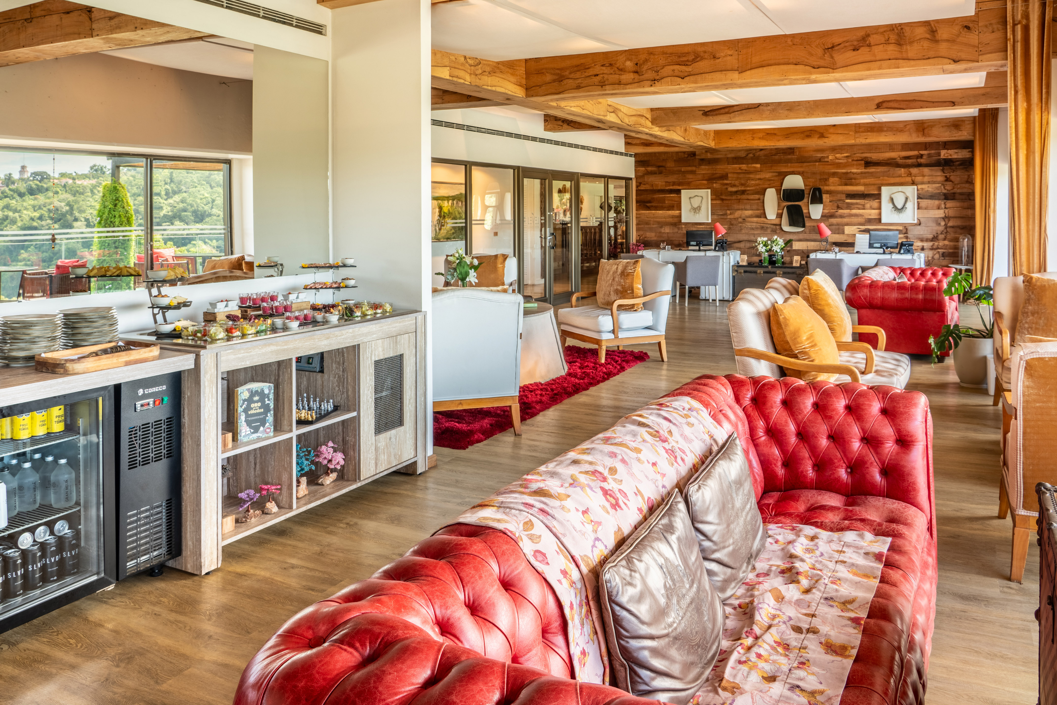Hotel lounge with red sofas, buffet, wooden beams, and scenic view.