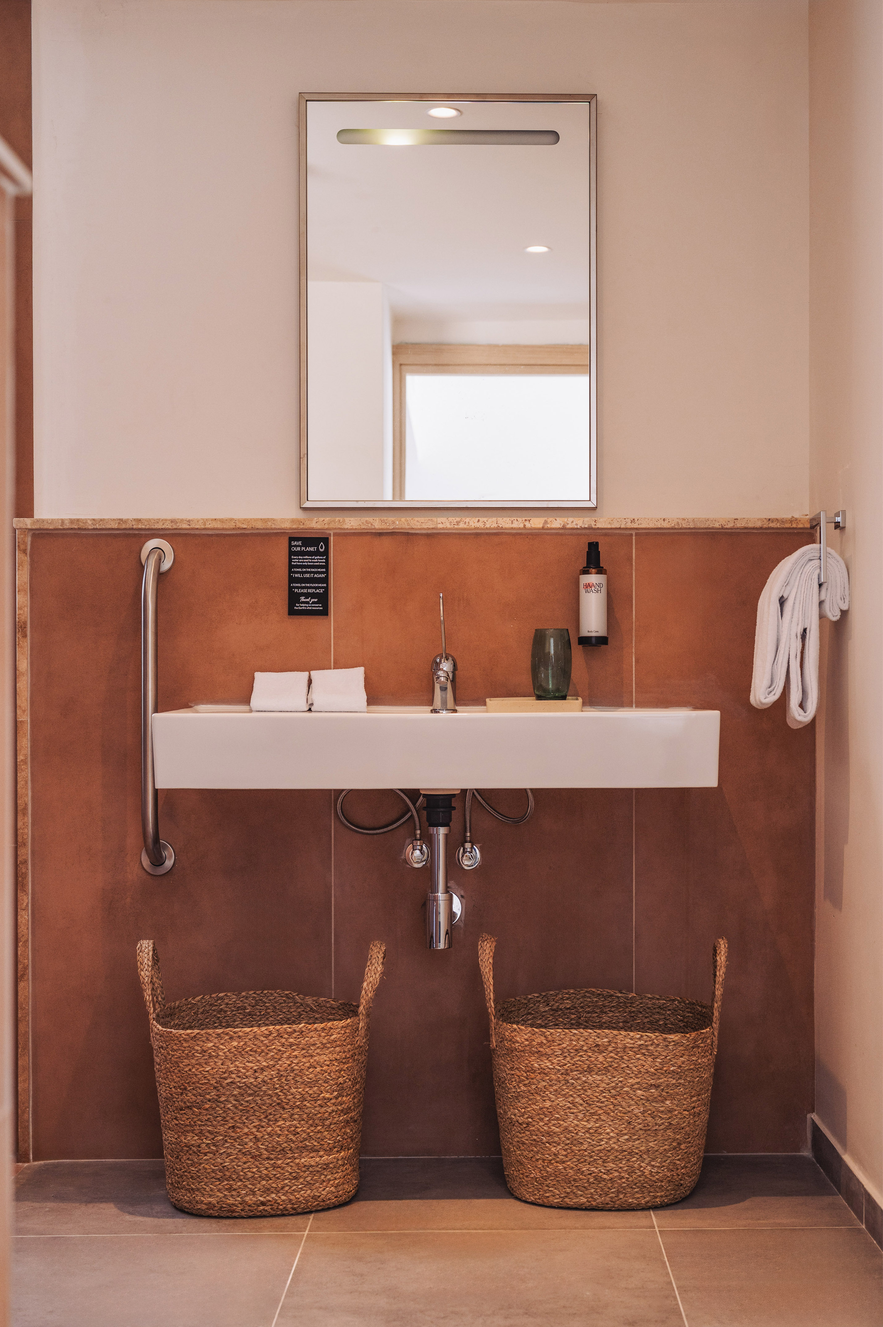 Accessible hotel bathroom vanity with sink, lighted mirror, terracotta tiles.